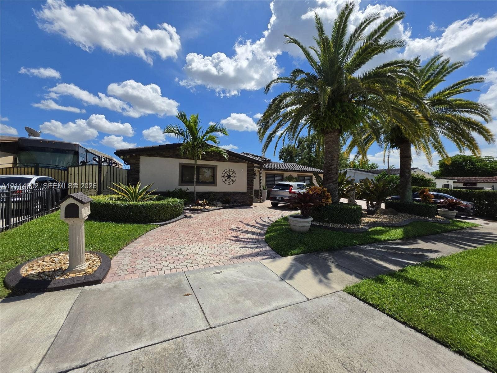 8450 NW 178th Street, Hialeah, Hialeah, FL 33015 Exterior facade featuring stone veneer detailing, expansive paver driveway, manicured landscaping, mature palm trees, and decorative wall accents