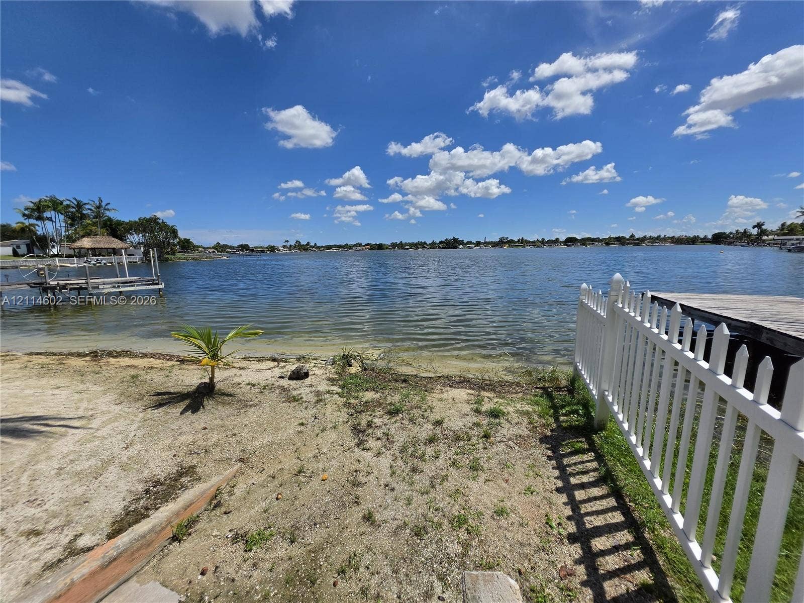 8450 NW 178th Street, Hialeah, Hialeah, FL 33015 Waterfront parcel featuring a sandy shoreline, private wooden dock, and white picket fencing