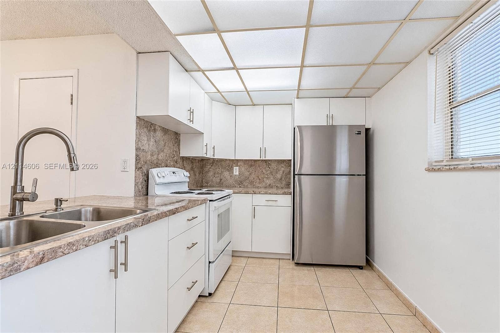 14155 SW 87th Street, #404-E, Miami, FL 33183 Kitchen featuring white cabinetry, stone-finish countertops, stainless steel refrigerator, tile flooring, and a drop-in sink with a high-arc faucet