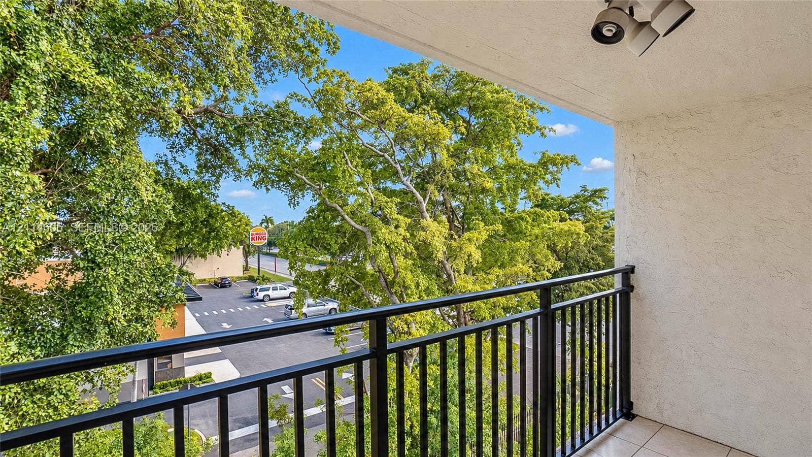 14155 SW 87th Street, #404-E, Miami, FL 33183 Covered balcony featuring textured stucco walls, tile flooring, a black metal railing, and overhead lighting