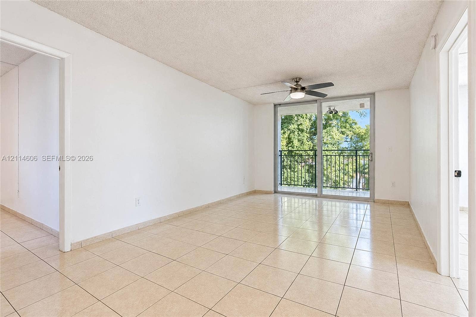 14155 SW 87th Street, #404-E, Miami, FL 33183 Open-concept interior featuring neutral tile flooring, ceiling fan with integrated lighting, and glass sliding doors providing access to a private balcony with metal railing