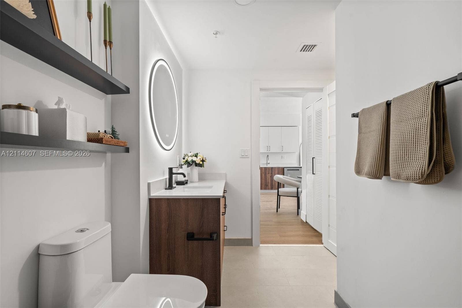 2479 NE 192nd Street, #103, Miami, Miami, FL 33180 Bathroom featuring a wood-finish vanity with a stone countertop, an integrated sink, a backlit circular mirror, matte black fixtures, and built-in wall shelving