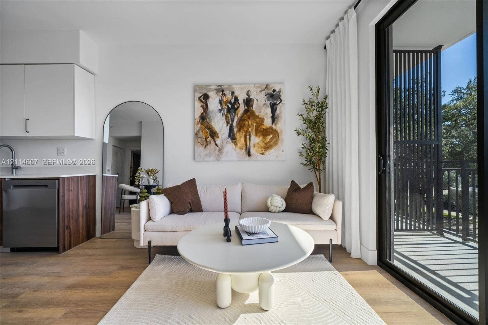 2479 NE 192nd Street, #103, Miami, Miami, FL 33180 Living area featuring wood-finish flooring, white cabinetry, integrated stainless steel appliances, and large sliding glass doors leading to a railed balcony