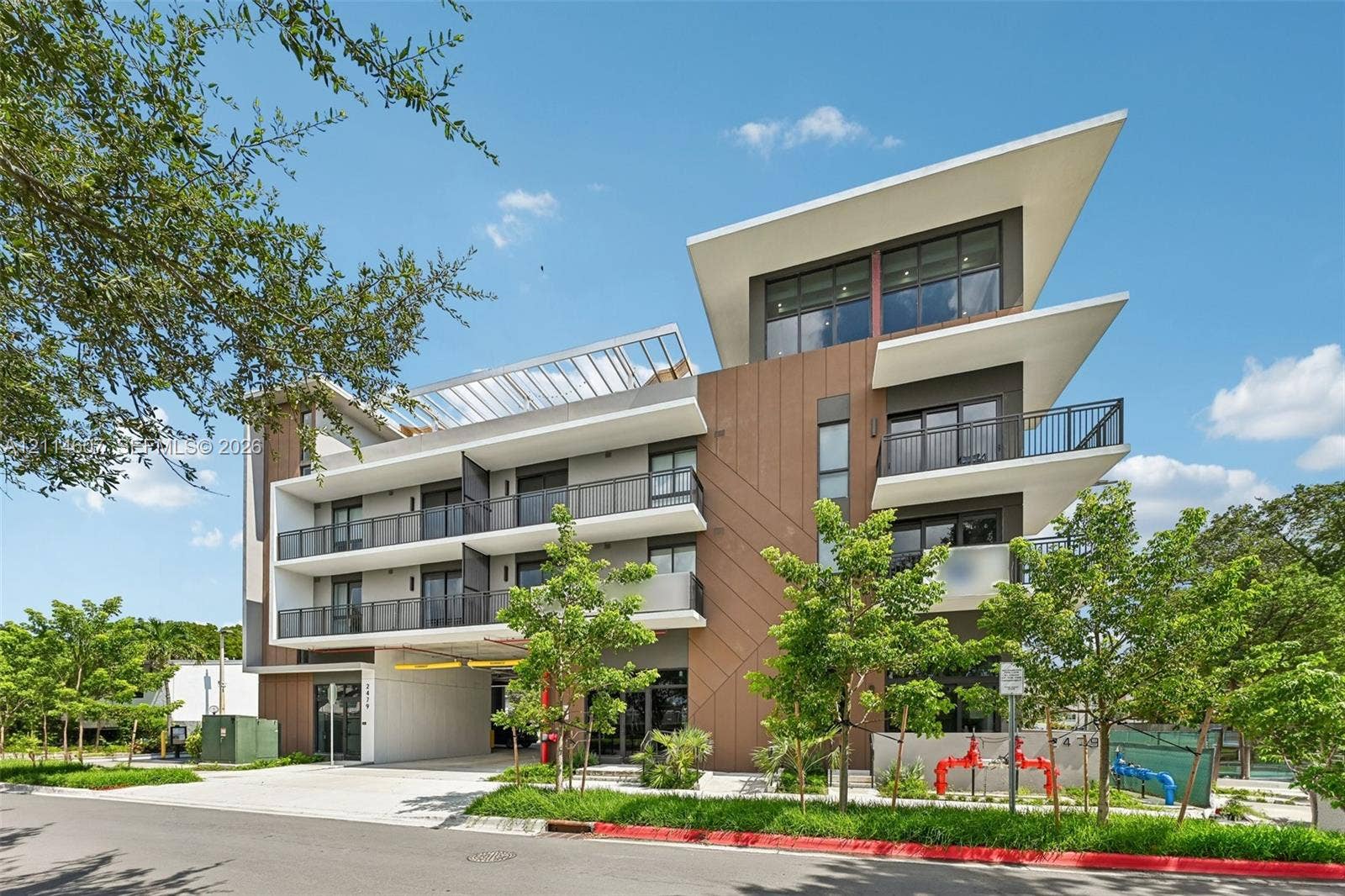 2479 NE 192nd Street, #103, Miami, Miami, FL 33180 Modern multi-level exterior featuring clean geometric lines, a shed-style roof, wood-tone paneling, metal balcony railings, and covered ground-level parking