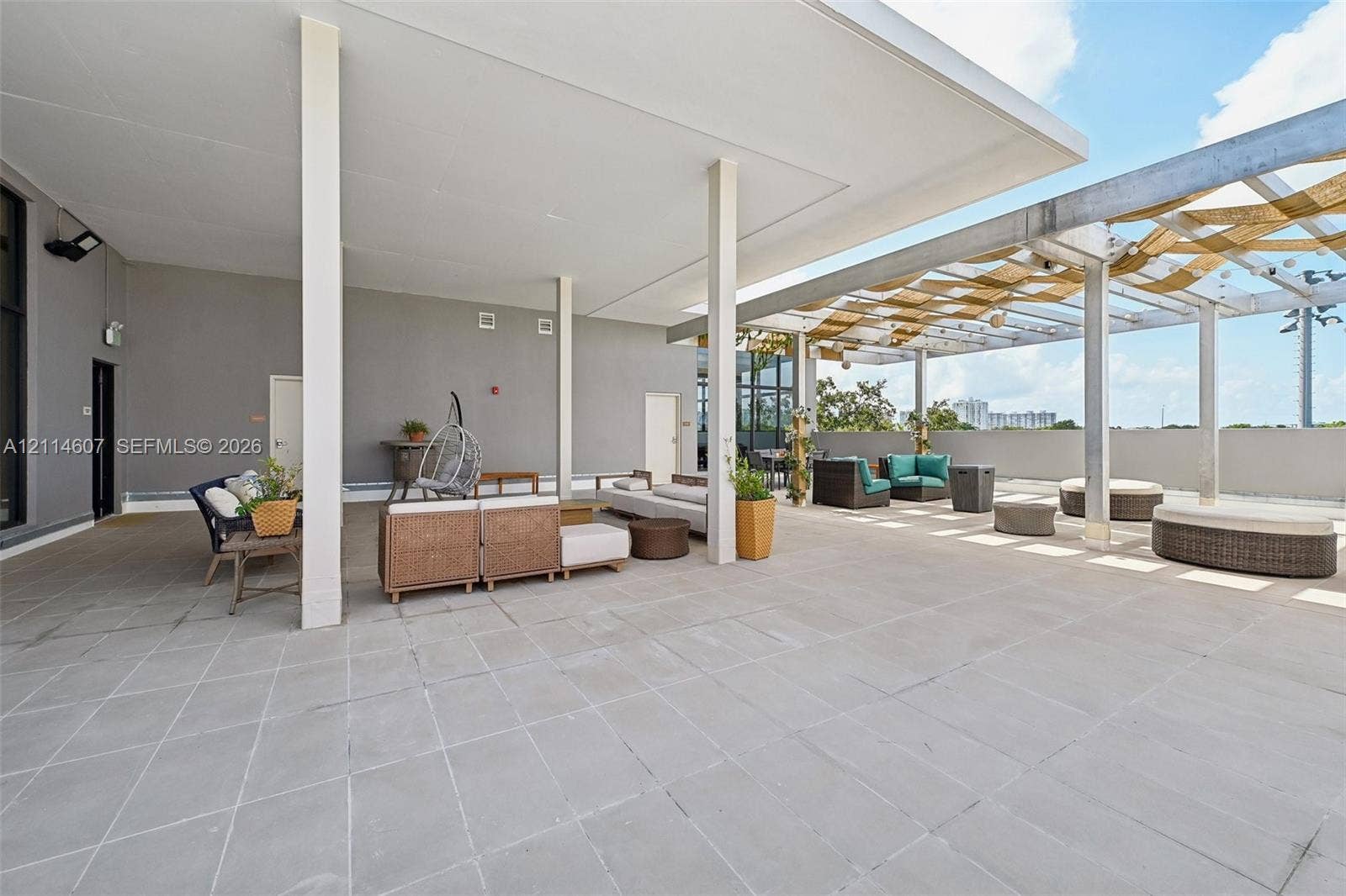 2479 NE 192nd Street, #103, Miami, Miami, FL 33180 Expansive rooftop terrace featuring large-format stone tile flooring, a covered patio section with structural support columns, and an open-air area with a metal pergola frame