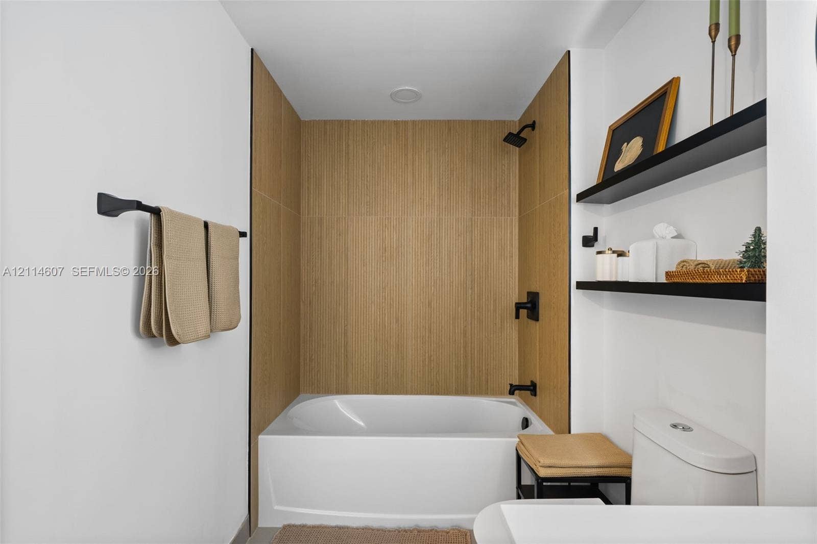 2479 NE 192nd Street, #103, Miami, Miami, FL 33180 Bathtub enclosure featuring light wood-finish tile surround, matte black plumbing fixtures, and two wall-mounted floating shelves