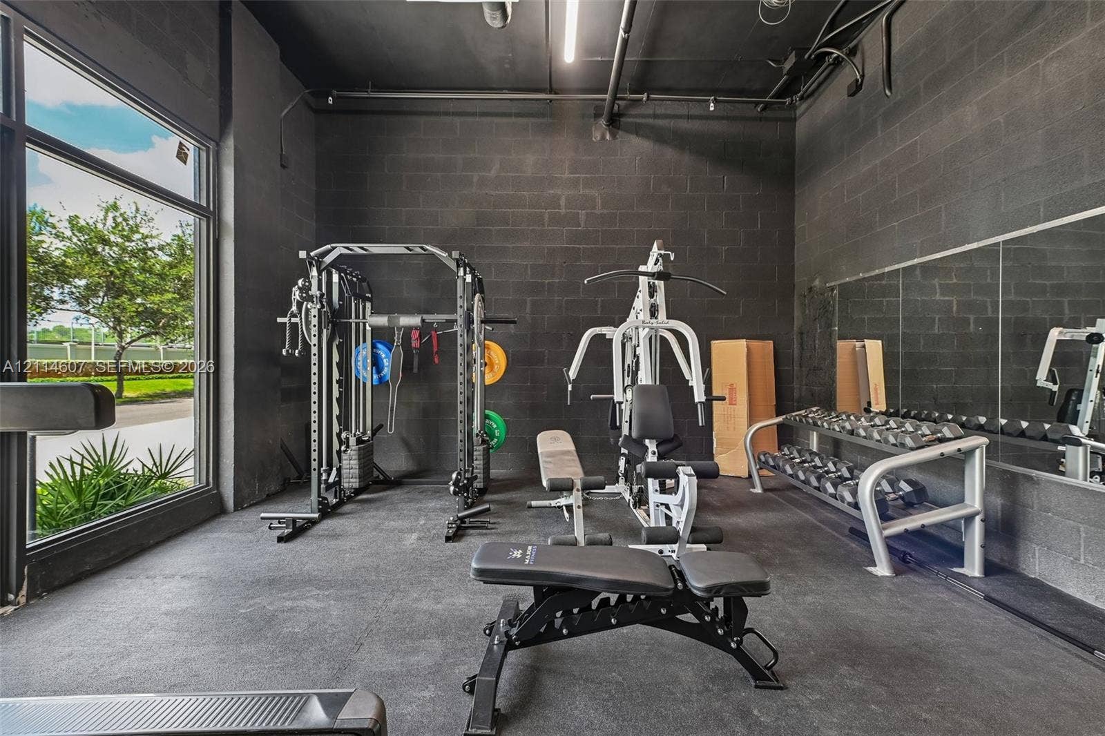 2479 NE 192nd Street, #103, Miami, Miami, FL 33180 Industrial-style interior space featuring exposed dark-painted concrete block walls, high ceilings with exposed mechanical conduits, floor-to-ceiling windows, and wall-to-wall mirrors