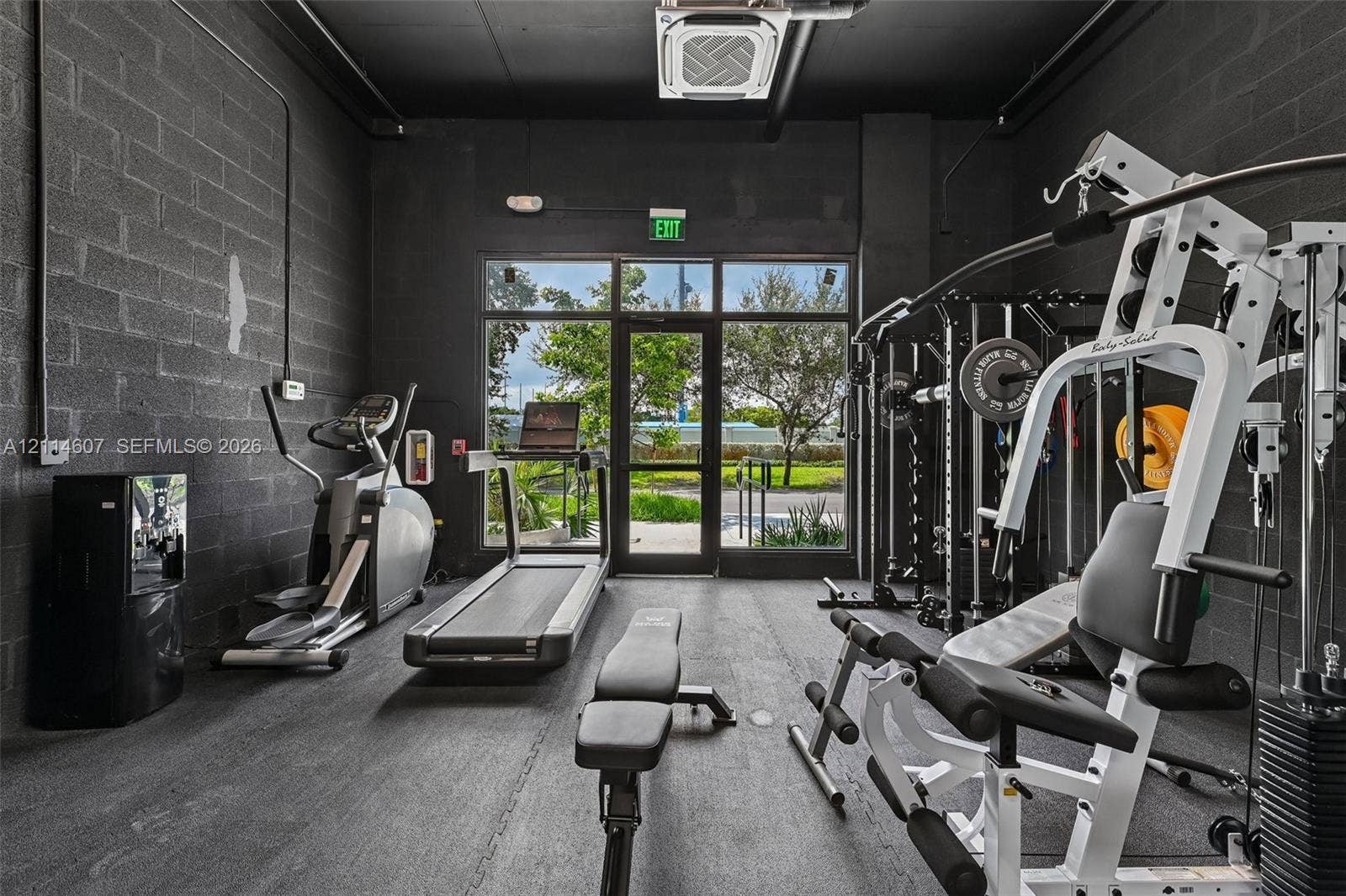 2479 NE 192nd Street, #103, Miami, Miami, FL 33180 Fitness area featuring painted concrete block walls, durable rubberized flooring, an exposed ceiling structure, and floor-to-ceiling glass paneling with an exterior door