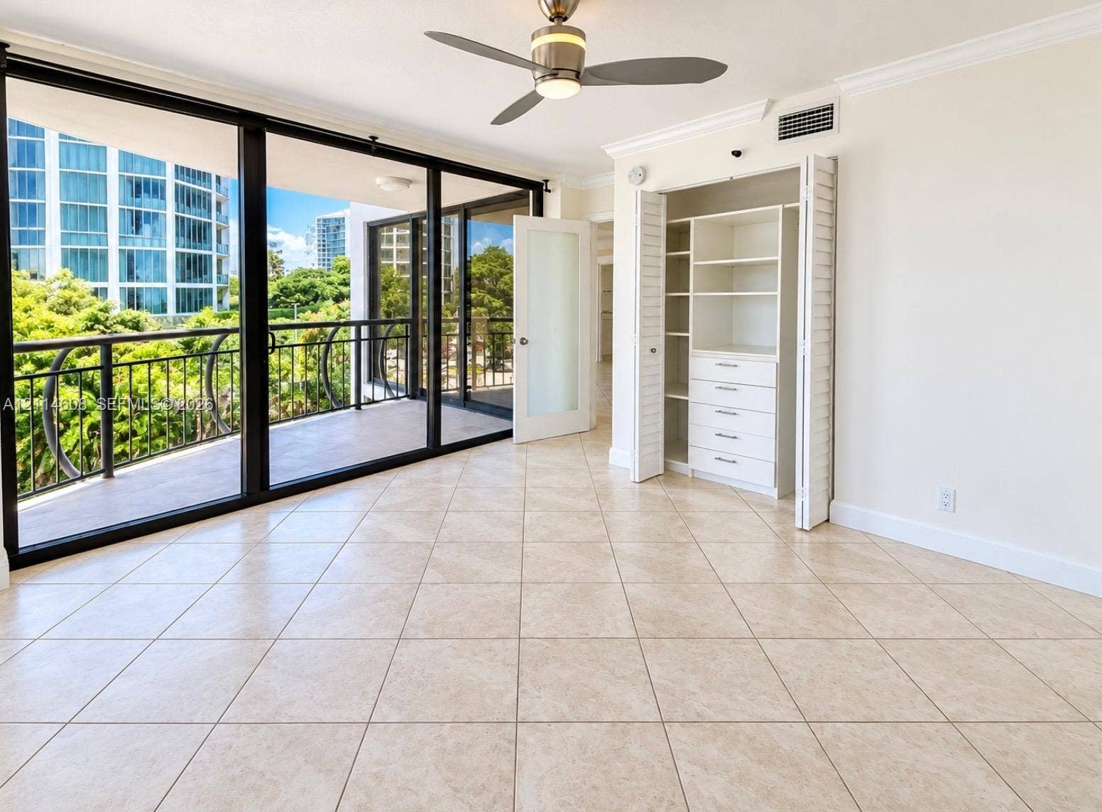 Floor-to-ceiling glass sliding doors, private balcony with metal railing, built-in closet with multi-drawer storage and shelving, ceramic tile flooring, and ceiling fan