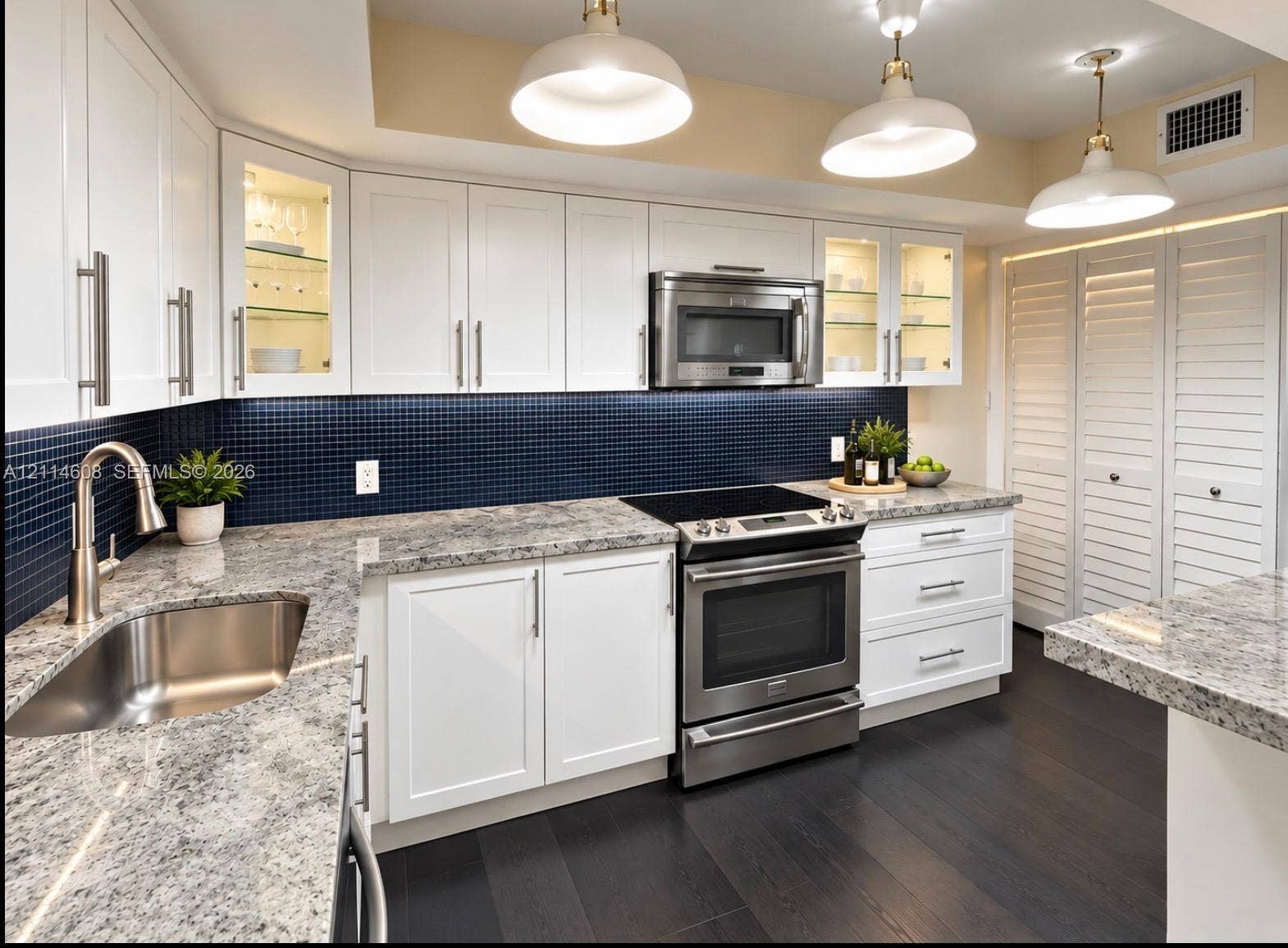 Kitchen featuring white shaker-style cabinetry, stone-surface countertops, blue mosaic tile backsplash, stainless steel appliances