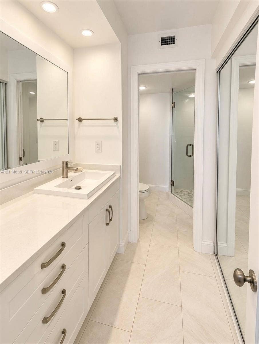 Bathroom vanity featuring white cabinetry, a rectangular vessel sink, and light-toned solid surface countertop, complemented by floor-to-ceiling mirrored closet doors