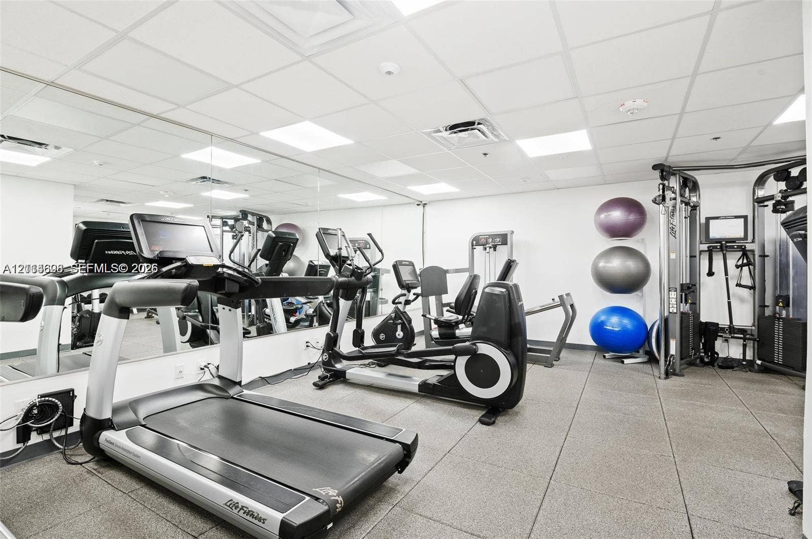 Fitness center featuring a wall-to-wall mirror, drop ceiling with recessed lighting, and durable rubberized tile flooring