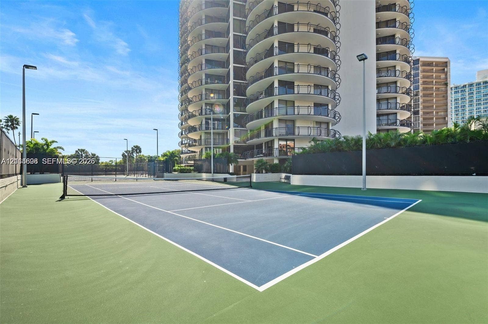 Hard-surface tennis court featuring perimeter fencing and overhead court lighting
