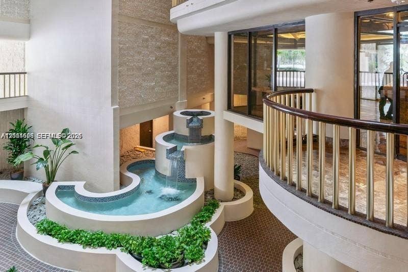 Multi-level atrium featuring a tiered stone fountain, curved staircase with wooden railing, stone flooring, and textured wall accents