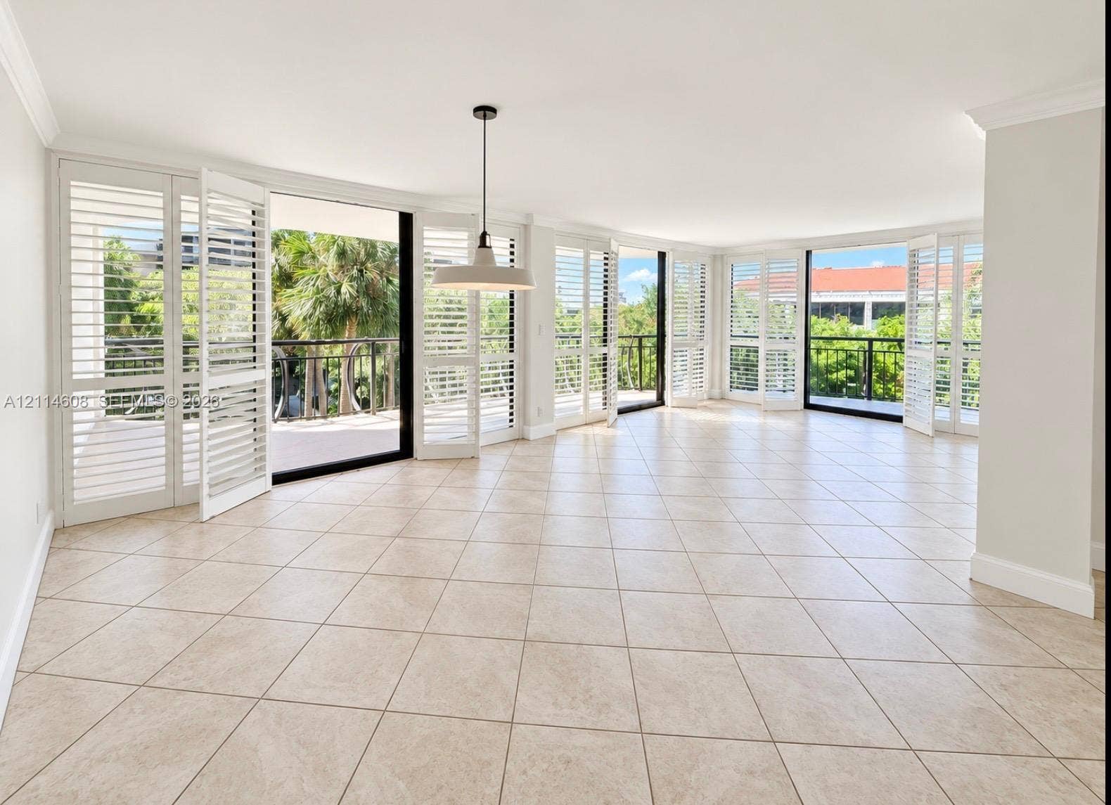 Open floor plan featuring light-toned tile flooring, floor-to-ceiling multi-panel glass doors, plantation shutters