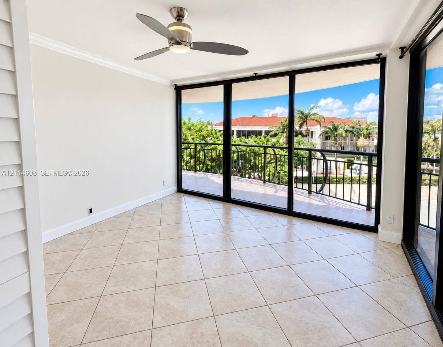 Floor-to-ceiling glass sliding doors, ceramic tile flooring, ceiling fan with integrated lighting, and an expansive covered balcony