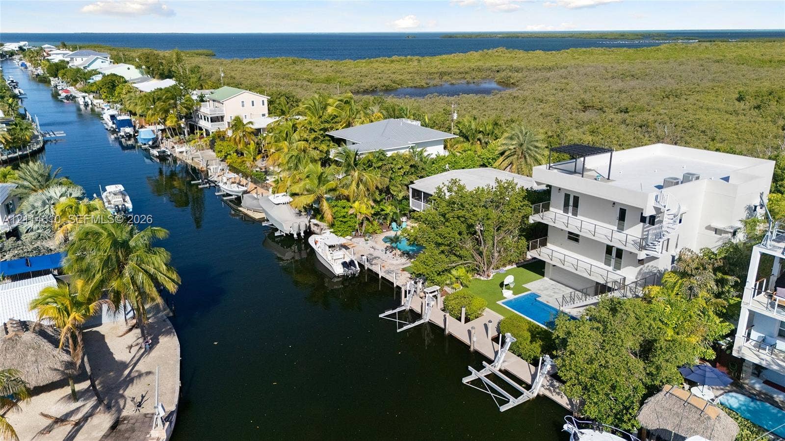 131 Ojibway Avenue, Islamorada, FL 33070 Three-story waterfront residence featuring a private boat dock, rectangular in-ground swimming pool, multi-level balconies with metal railings, and a rooftop terrace