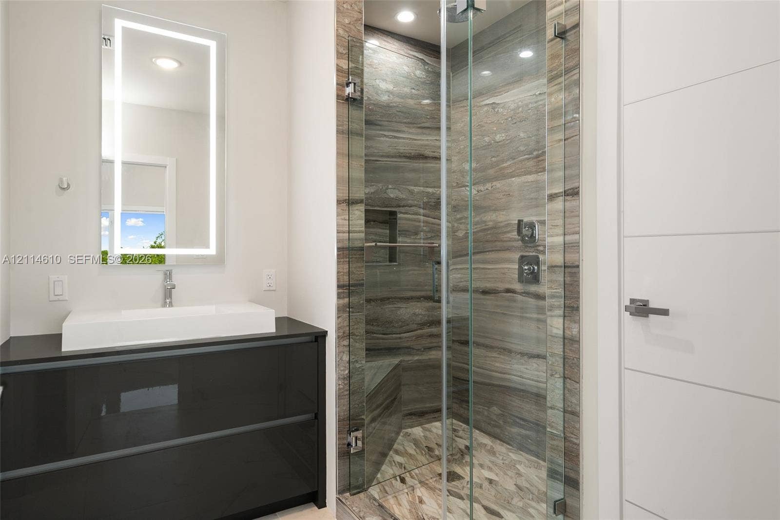 131 Ojibway Avenue, Islamorada, FL 33070 Floating dark-finish vanity with rectangular vessel sink, LED-integrated mirror, walk-in shower with floor-to-ceiling stone-patterned tile, glass shower enclosure, and built-in shower bench