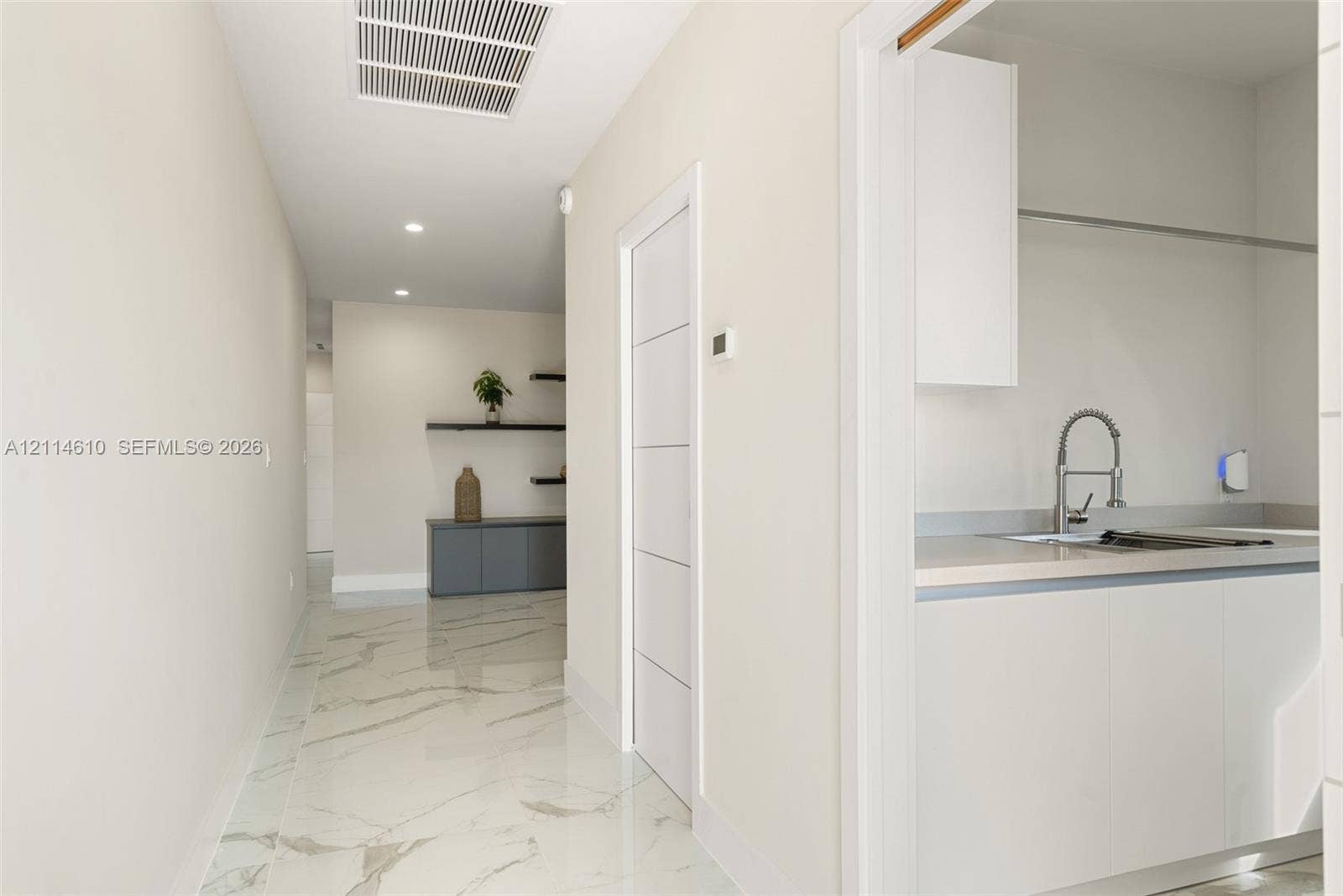 131 Ojibway Avenue, Islamorada, FL 33070 Hallway featuring polished stone-finish flooring with veining detail, recessed ceiling lighting, a five-panel interior door, and built-in cabinetry with wall-mounted shelving