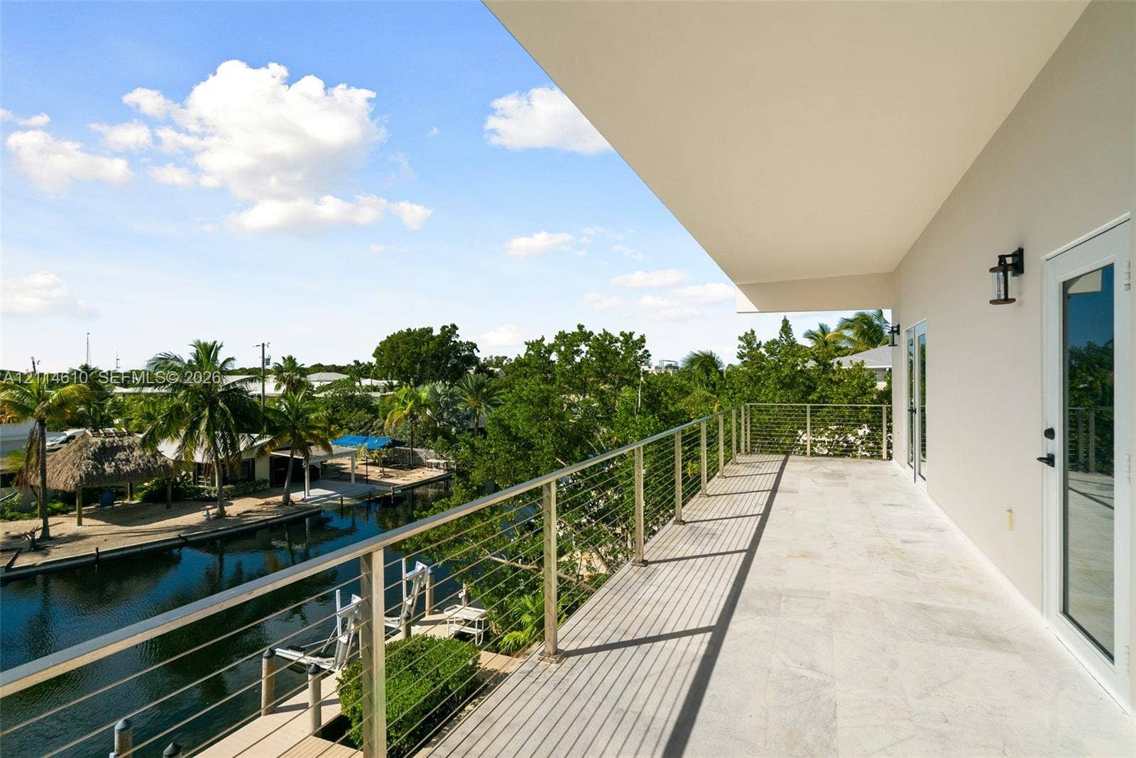 131 Ojibway Avenue, Islamorada, FL 33070 Covered balcony featuring stone flooring, a stainless steel cable railing system, and wall-mounted exterior lighting