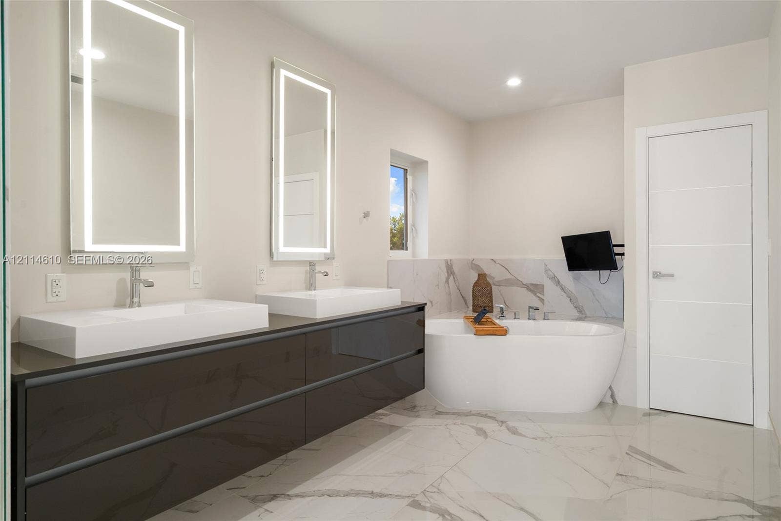 131 Ojibway Avenue, Islamorada, FL 33070 Floating dual vanity with integrated rectangular sinks, backlit wall-mounted mirrors, freestanding soaking tub, and large-format tile flooring with veining detail