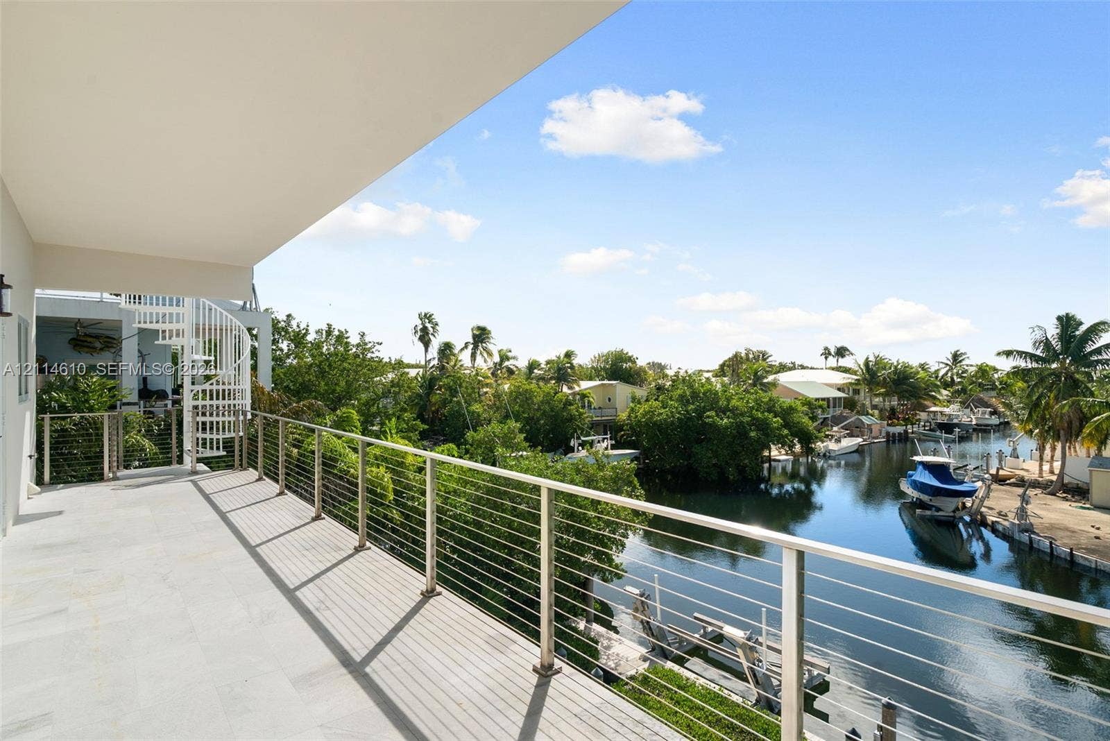 131 Ojibway Avenue, Islamorada, FL 33070 Covered balcony featuring stone-finish flooring, a white metal spiral staircase, and a stainless steel cable railing system overlooking a canal