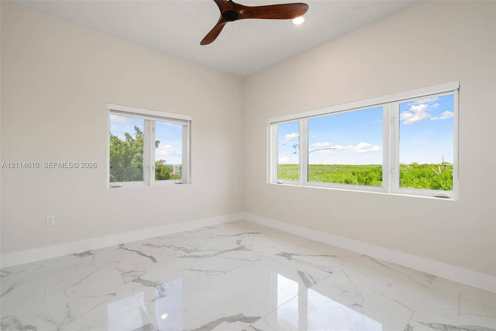 131 Ojibway Avenue, Islamorada, FL 33070 High-ceiling room featuring large windows with landscape scenery, polished stone-finish flooring, and a ceiling fan with wood-finish blades