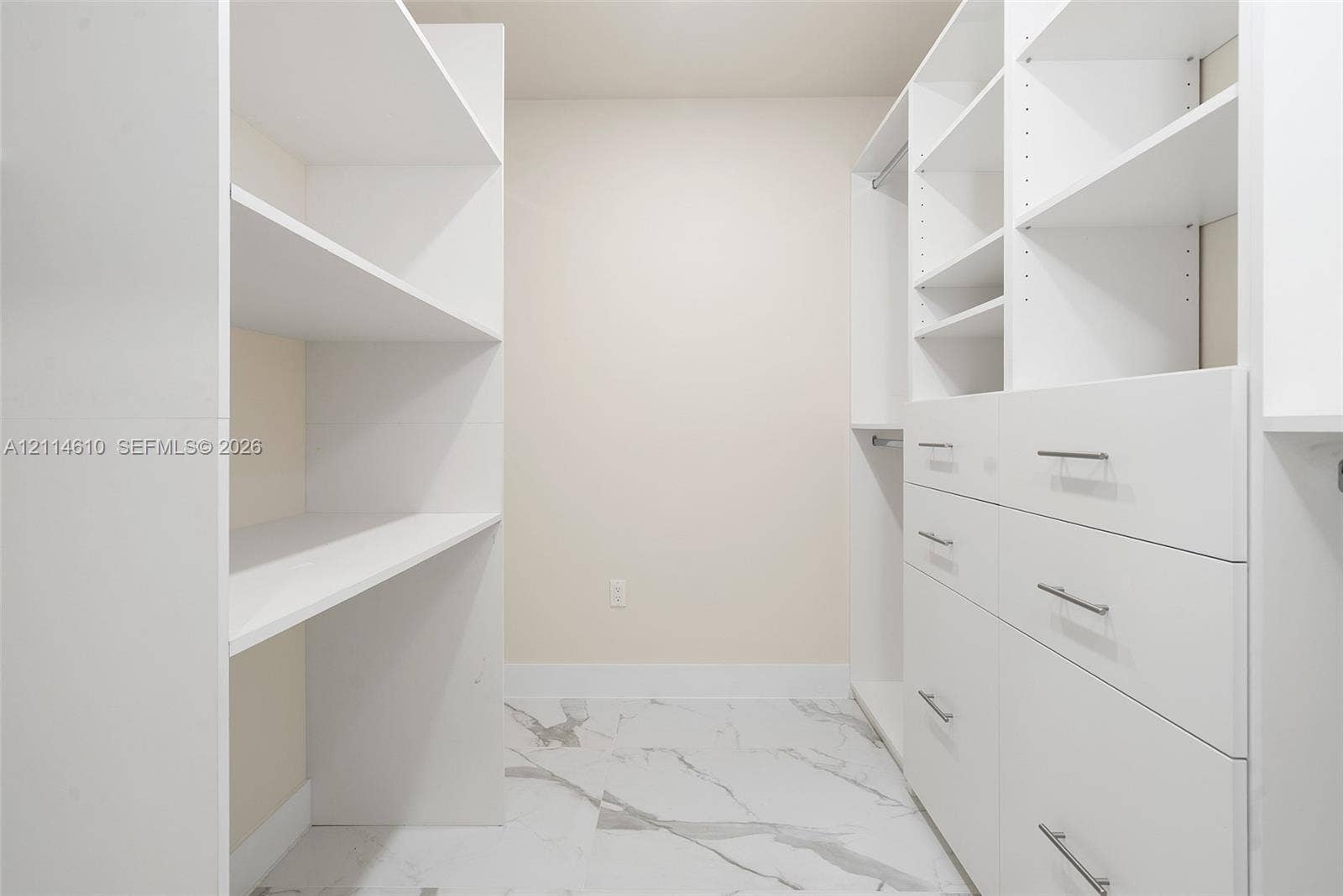 131 Ojibway Avenue, Islamorada, FL 33070 Walk-in closet featuring white custom built-in shelving, integrated hanging rods, and multi-drawer cabinetry with metallic pulls finished in polished chrome, complemented by large-format stone-pattern tile flooring