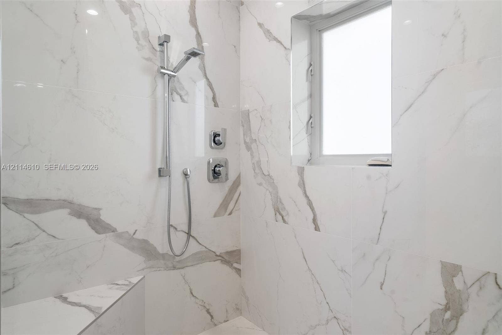 131 Ojibway Avenue, Islamorada, FL 33070 Walk-in shower featuring large-format veined tile surround, polished chrome adjustable handheld shower fixture, integrated tiled bench, and a rectangular transom window