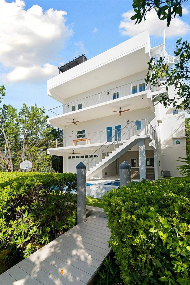 131 Ojibway Avenue, Islamorada, FL 33070 Multi-story exterior featuring stacked balconies with glass railings, an integrated swimming pool, a private dock with pilings, and an external staircase