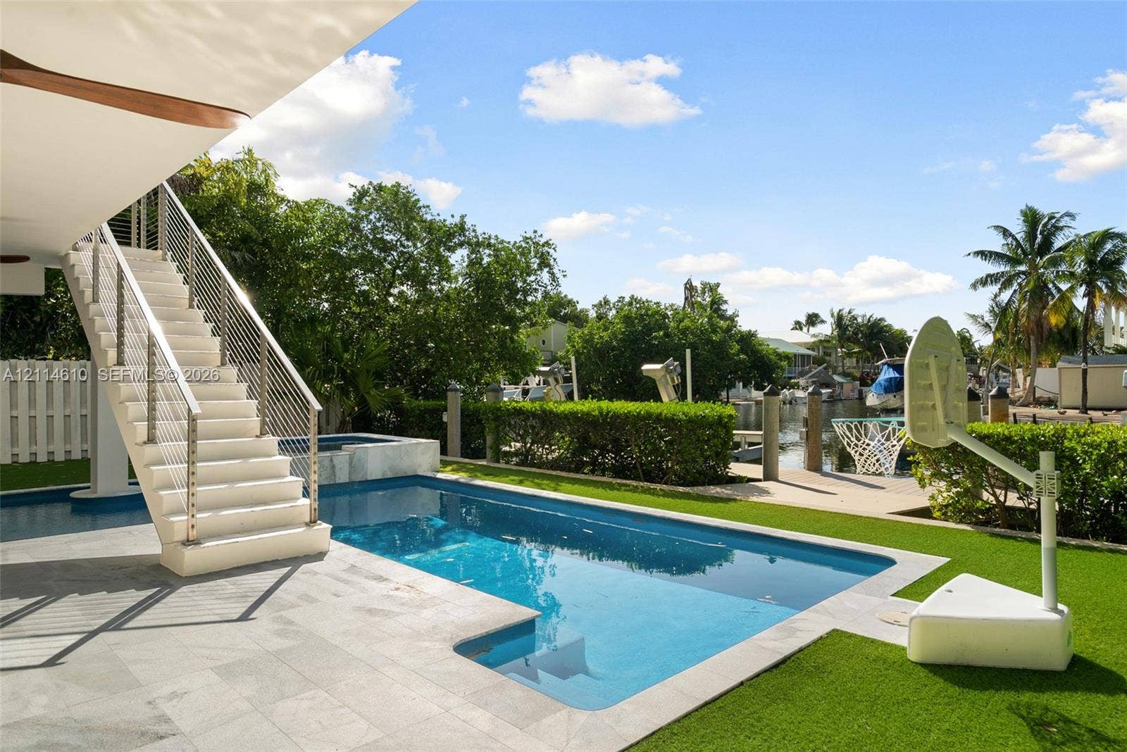 131 Ojibway Avenue, Islamorada, FL 33070 Outdoor living space featuring an in-ground swimming pool, stone-paver decking, elevated staircase with stainless steel cable railing, and direct water frontage with private boat slips