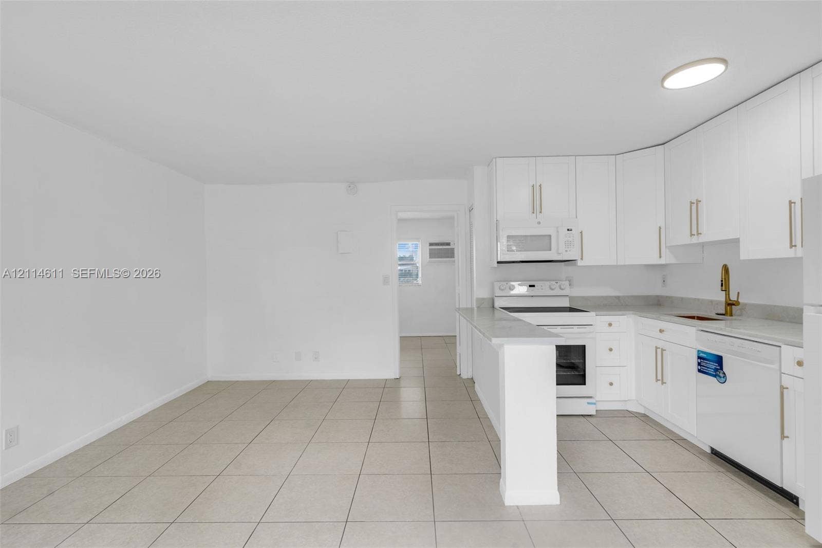 Kitchen featuring white shaker-style cabinetry, a gold-tone faucet, tiled flooring, and a peninsula counter