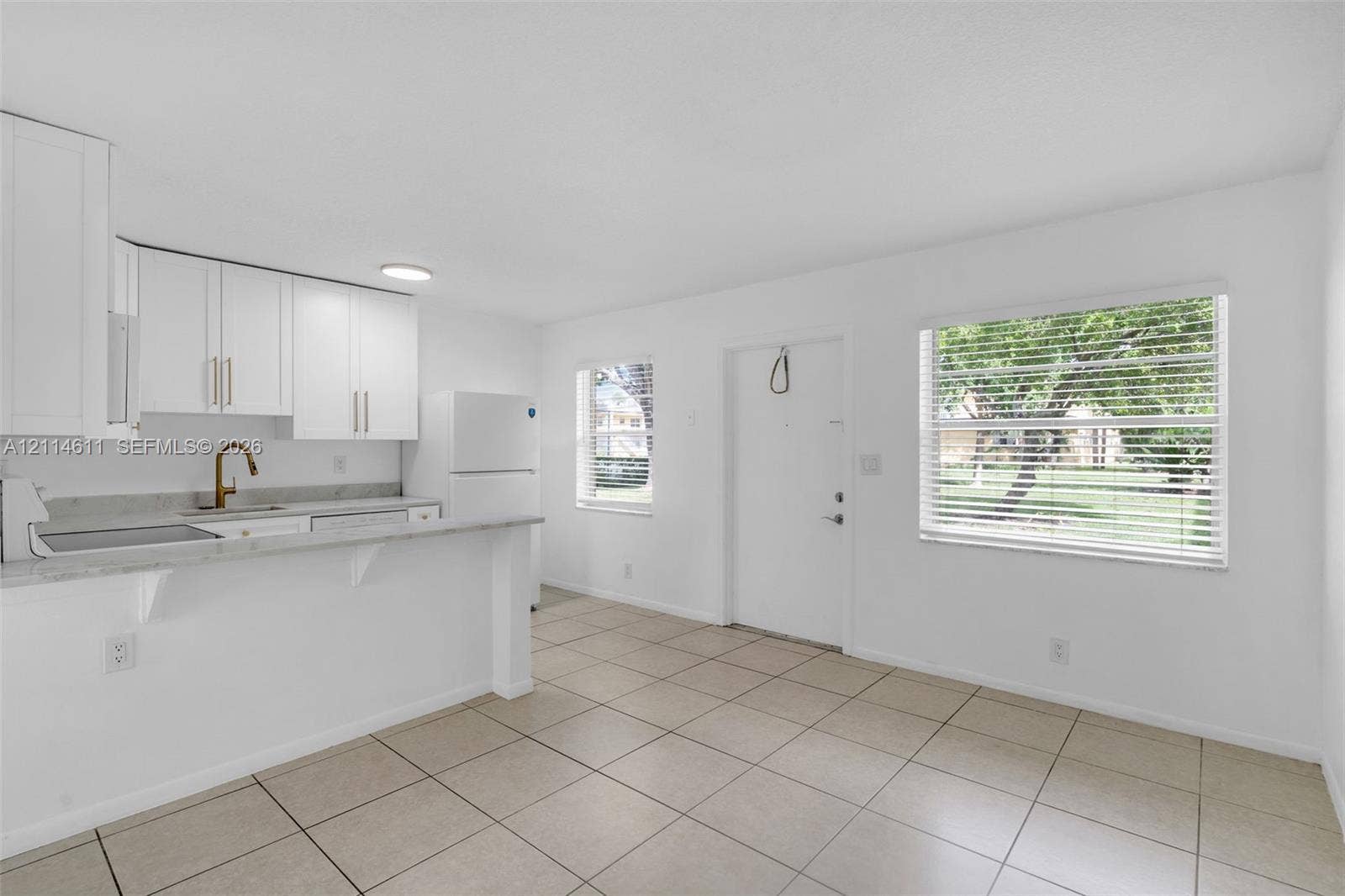 Kitchen featuring white cabinetry, stone-finish countertops, an under-mount sink with a bronze-tone faucet, and tile flooring