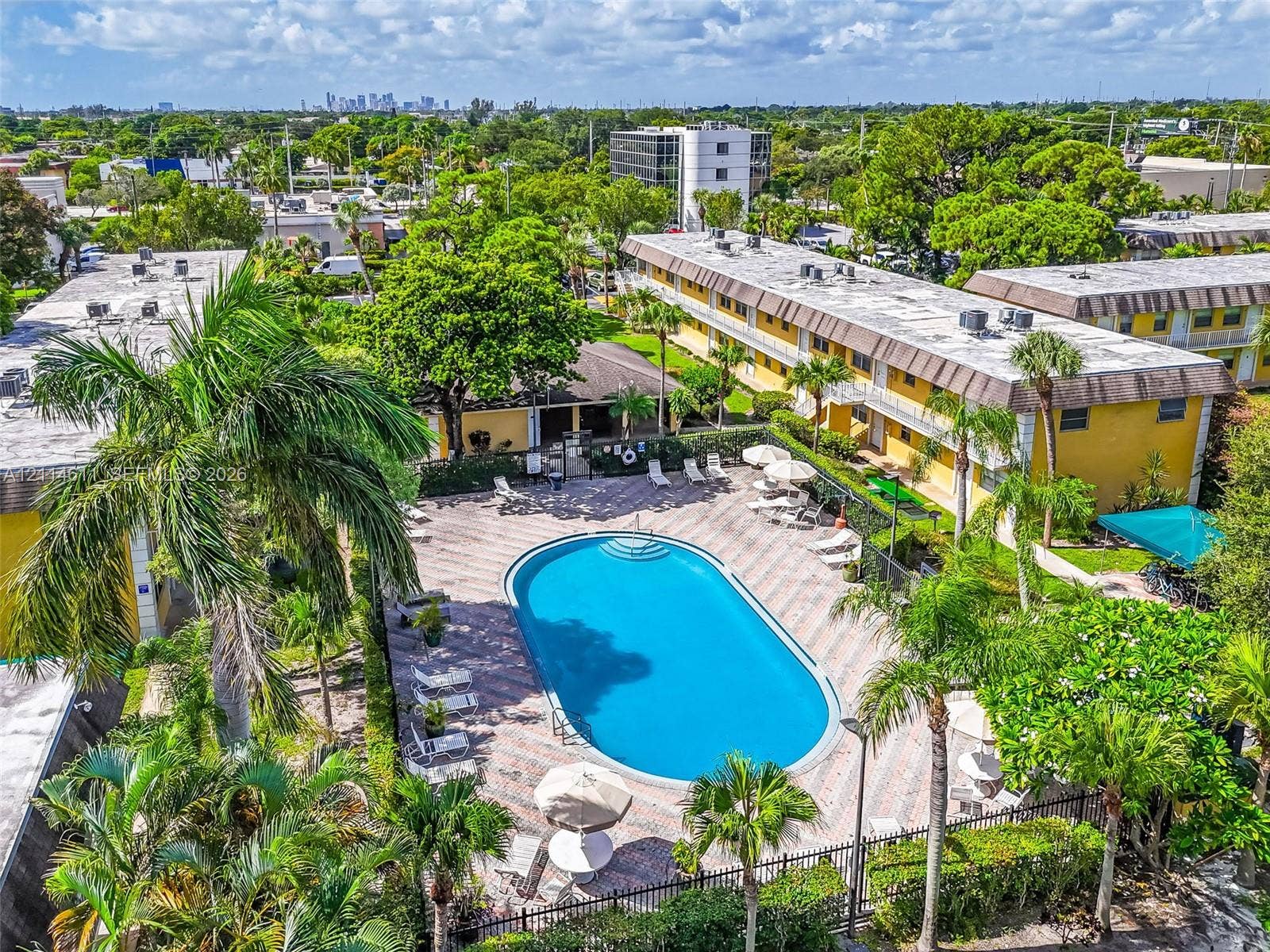 Aerial perspective of the common grounds featuring an oval swimming pool, paver-surfaced pool deck, established palm trees, and mature landscaping