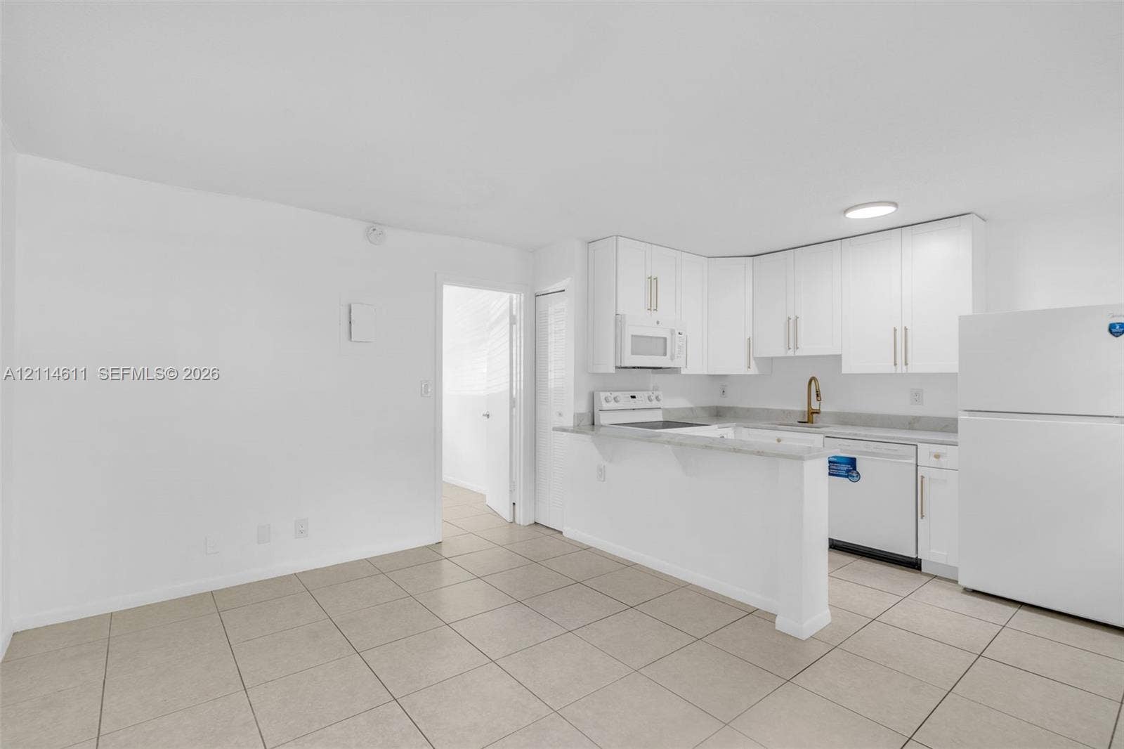 Kitchen featuring white cabinetry, solid-surface countertops, tile flooring, integrated appliances, and a brass-finish faucet