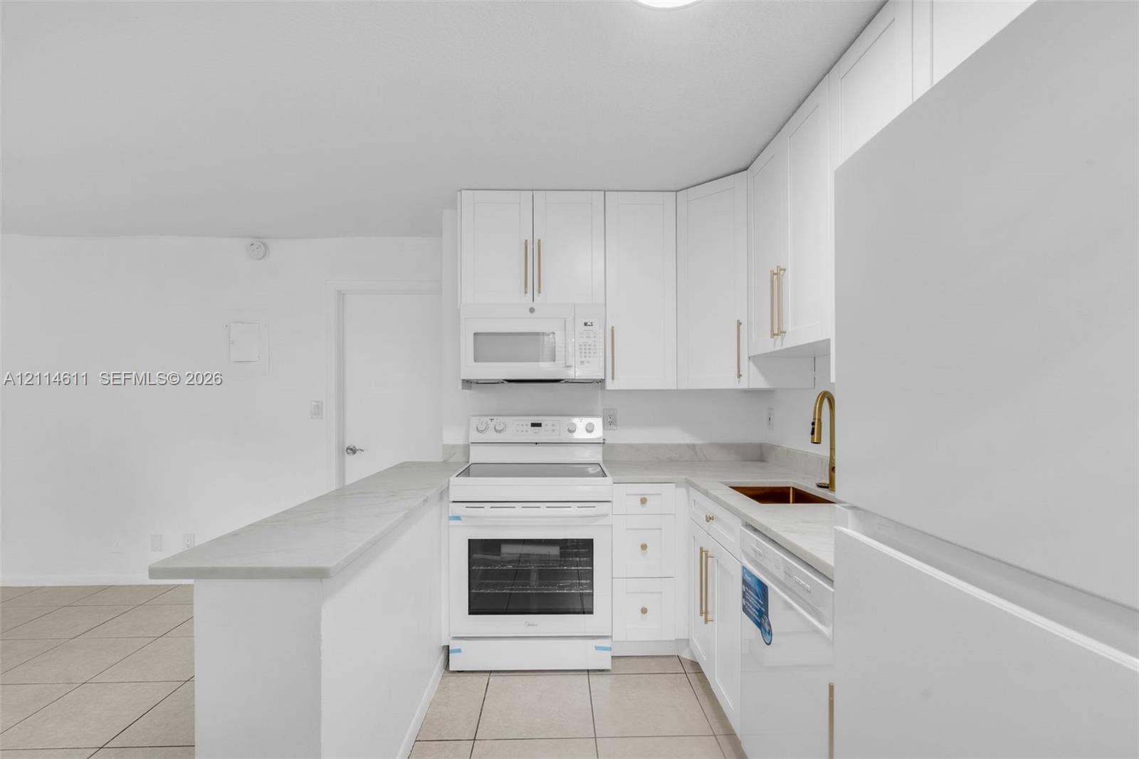 Kitchen featuring white shaker-style cabinetry, a stone-finish countertop, white electric range with matching over-the-range microwave, gold-tone faucet hardware, and ceramic tile flooring