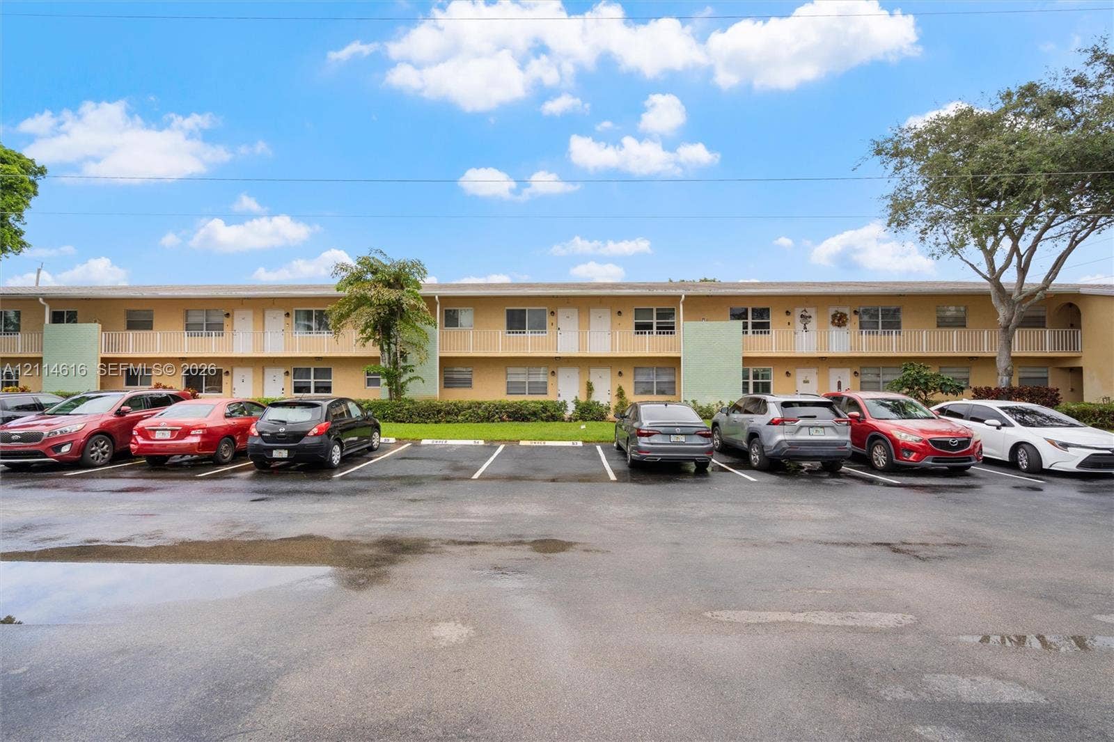 2607 NE 8th Avenue, #35, Wilton Manors, FL 33334 Two-story exterior featuring tan stucco siding, white balcony railings, and a paved parking lot with designated spaces