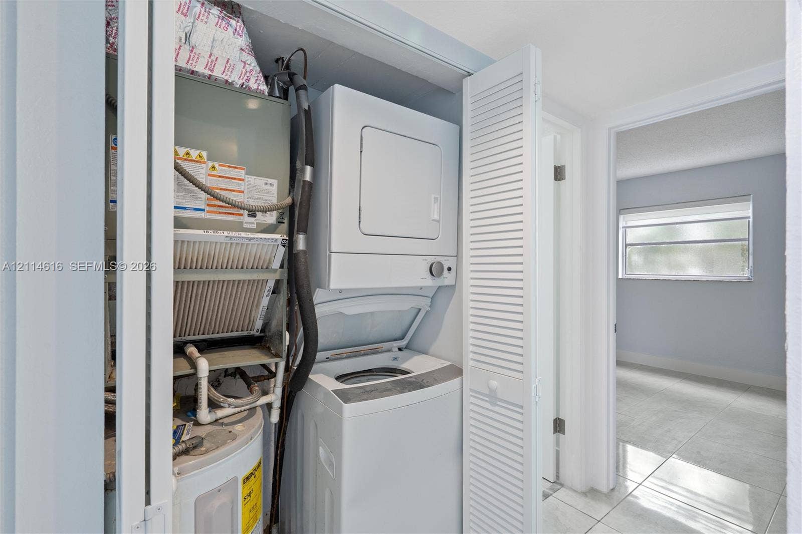 2607 NE 8th Avenue, #35, Wilton Manors, FL 33334 Utility closet featuring a stacked laundry appliance, water heater, HVAC air handler, and white louvered folding doors