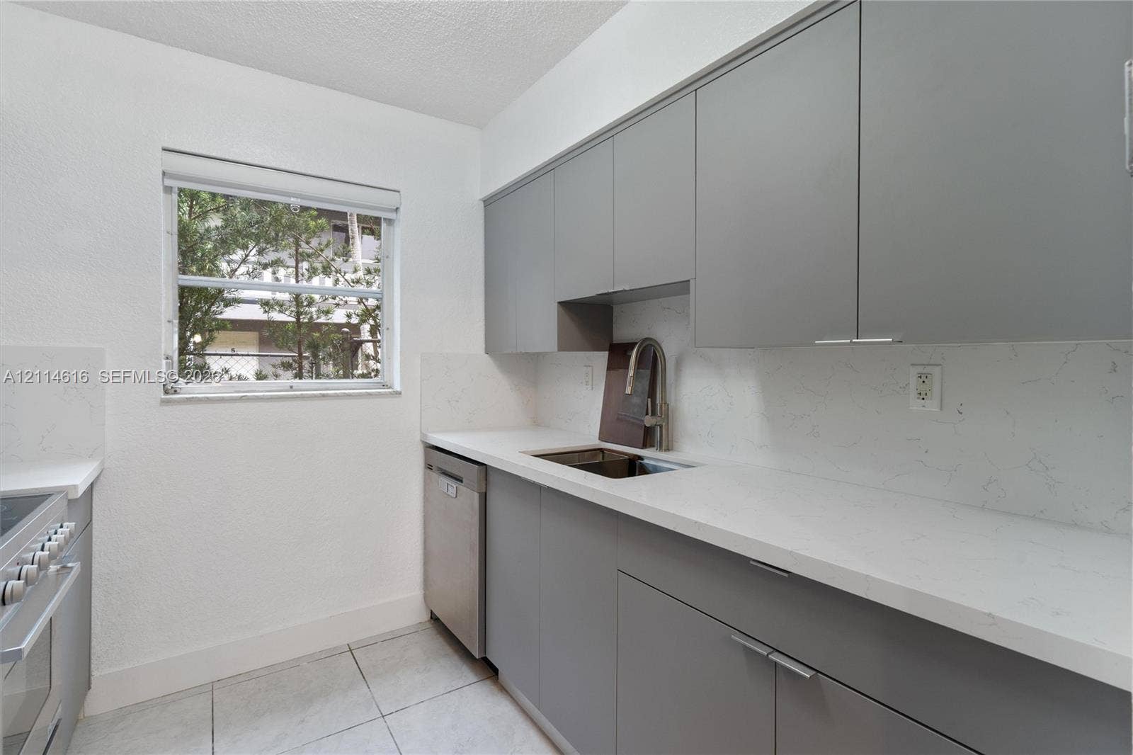 2607 NE 8th Avenue, #35, Wilton Manors, FL 33334 Kitchen featuring flat-panel gray cabinetry, solid-surface countertops with integrated backsplash, stainless steel dishwasher, and stainless steel pull-down faucet