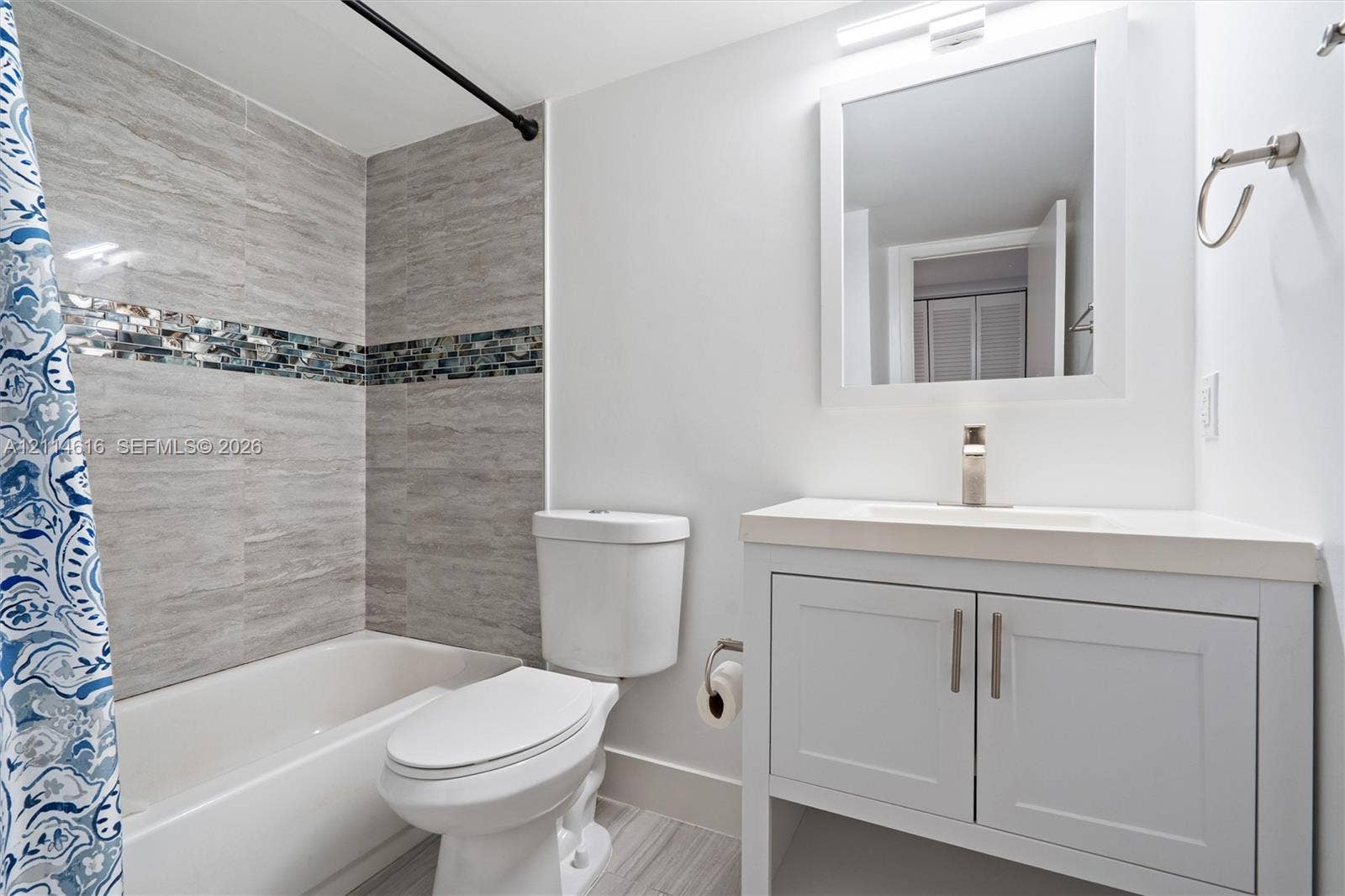 2607 NE 8th Avenue, #35, Wilton Manors, FL 33334 Bathroom featuring a vanity with shaker-style cabinetry and a single-basin countertop, a framed wall mirror, and a shower-tub combination accented with horizontal stone-finish tile and a decorative mosaic inlay