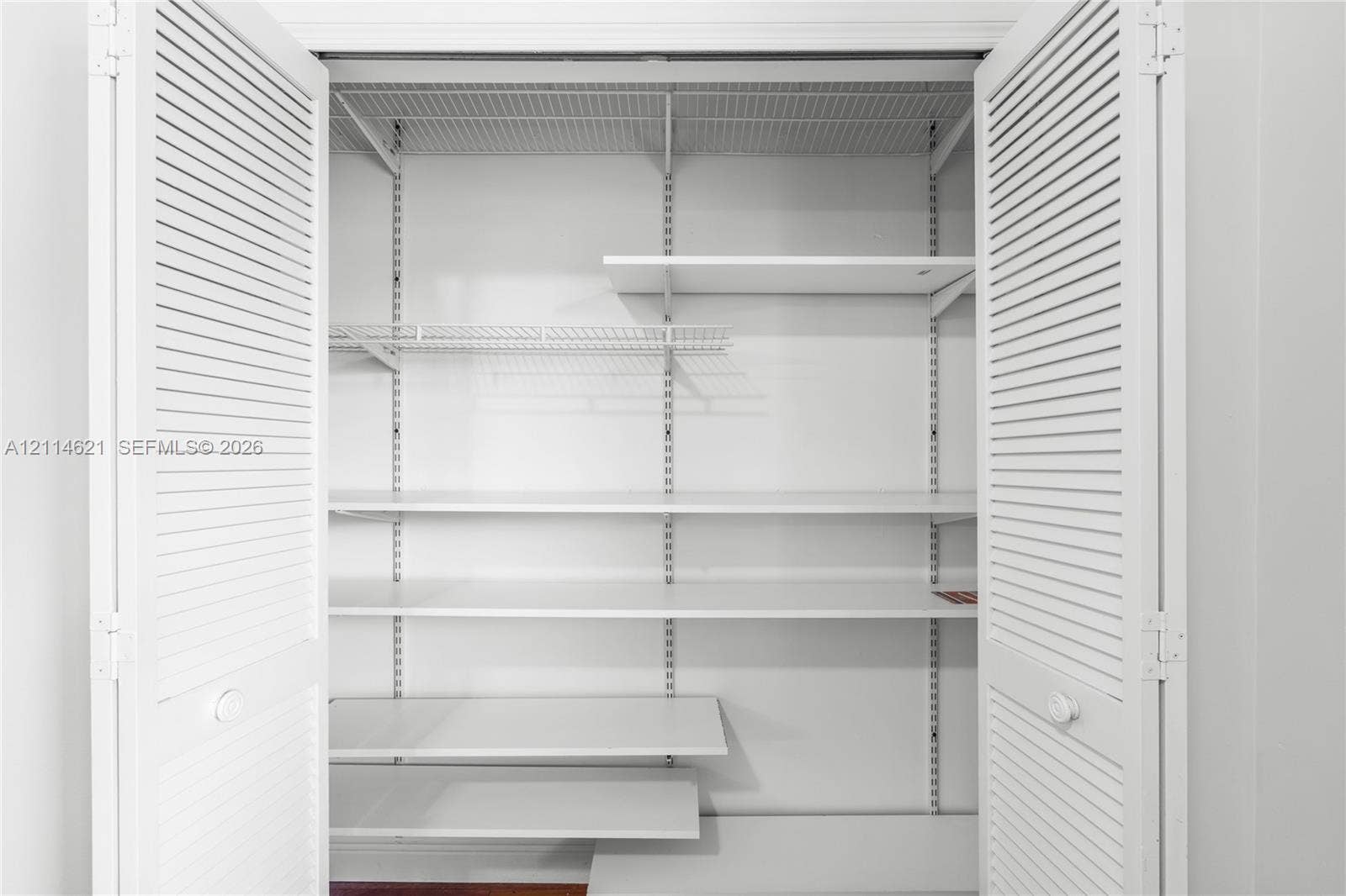 8978 NW 152nd Lane, #8978, Miami Lakes, Miami Lakes, FL 33018 Storage closet featuring white louvered bifold doors, adjustable shelving tracks, and multiple solid surface shelves