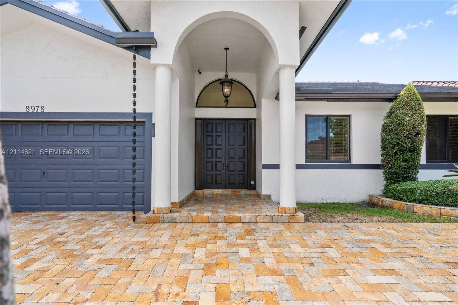8978 NW 152nd Lane, #8978, Miami Lakes, Miami Lakes, FL 33018 Exterior facade featuring a herringbone-patterned paver driveway, arched entryway with dual columns, double front doors with a semi-circular transom window, and a metal chain-link downspout