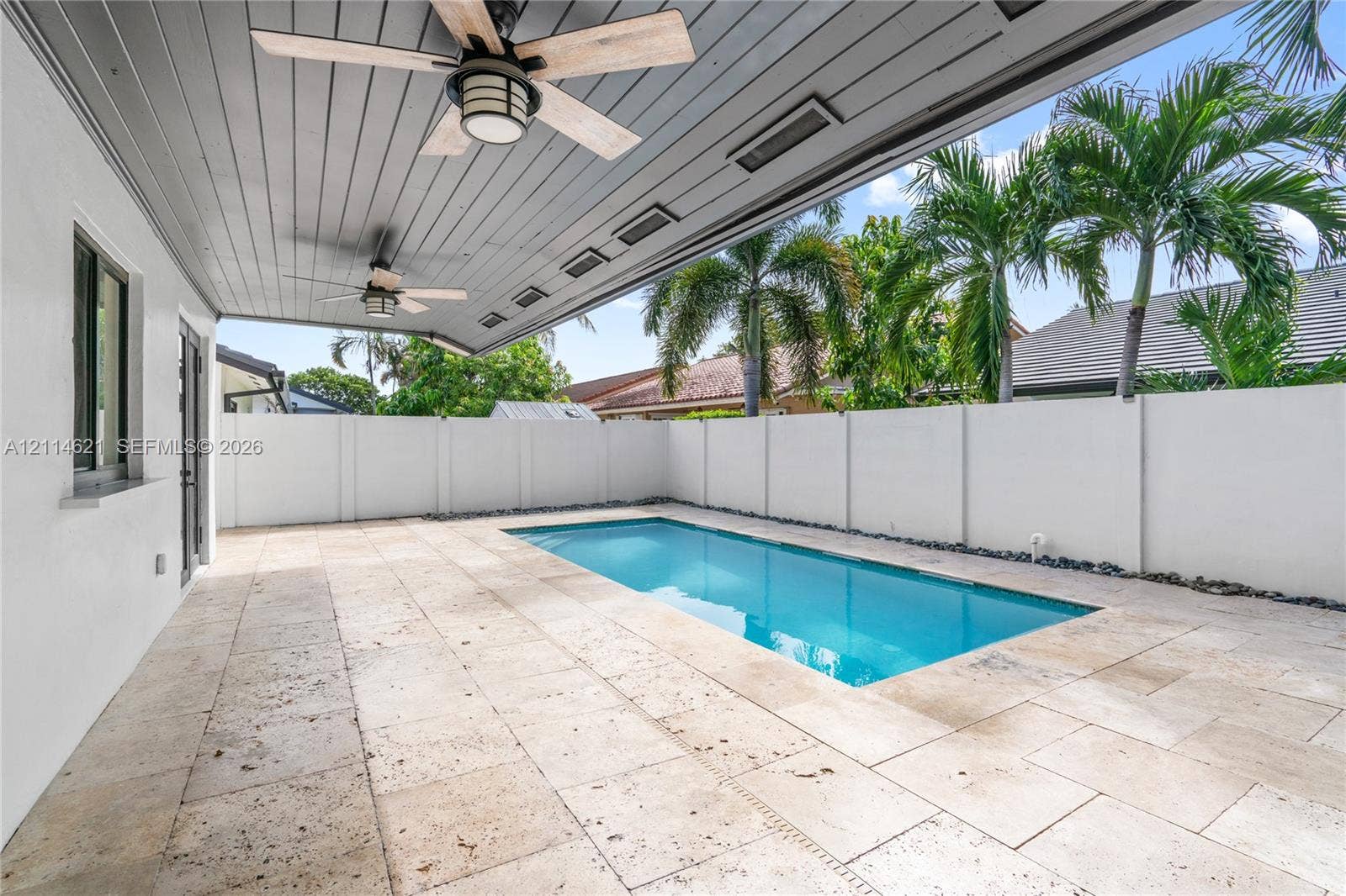 8978 NW 152nd Lane, #8978, Miami Lakes, Miami Lakes, FL 33018 Covered patio featuring a grey tongue-and-groove ceiling with dual ceiling fans, stone paver decking, and a rectangular swimming pool enclosed by a white privacy wall