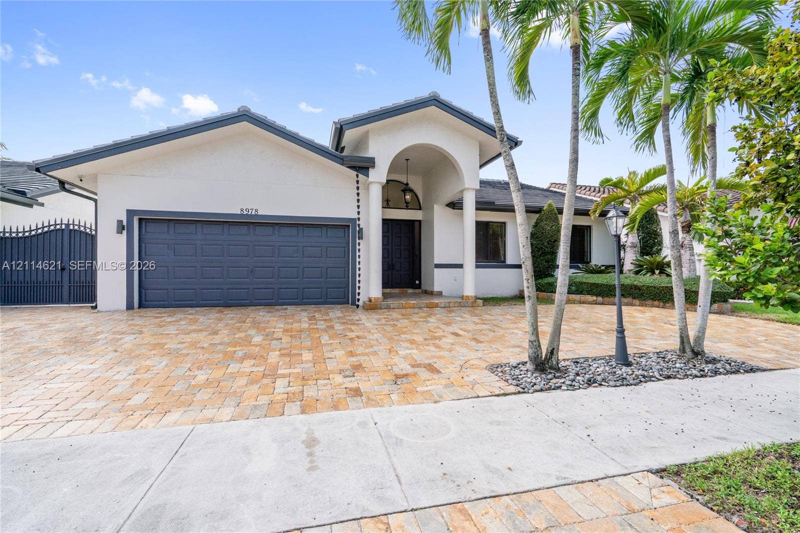 8978 NW 152nd Lane, #8978, Miami Lakes, Miami Lakes, FL 33018 Single-story residence featuring a paver driveway, arched entryway, multi-panel garage door, and mature landscaping