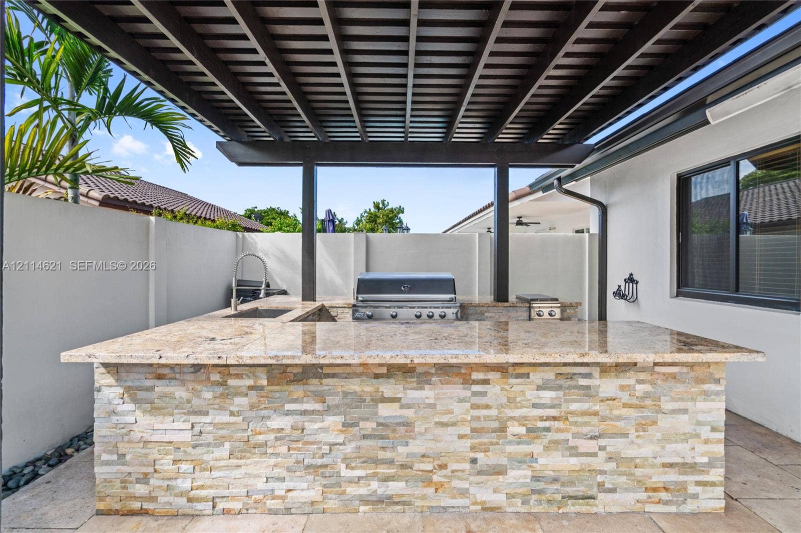 8978 NW 152nd Lane, #8978, Miami Lakes, Miami Lakes, FL 33018 Outdoor kitchen featuring a stacked-stone base, natural stone countertop, built-in stainless steel grill, integrated sink, and a covered pergola structure