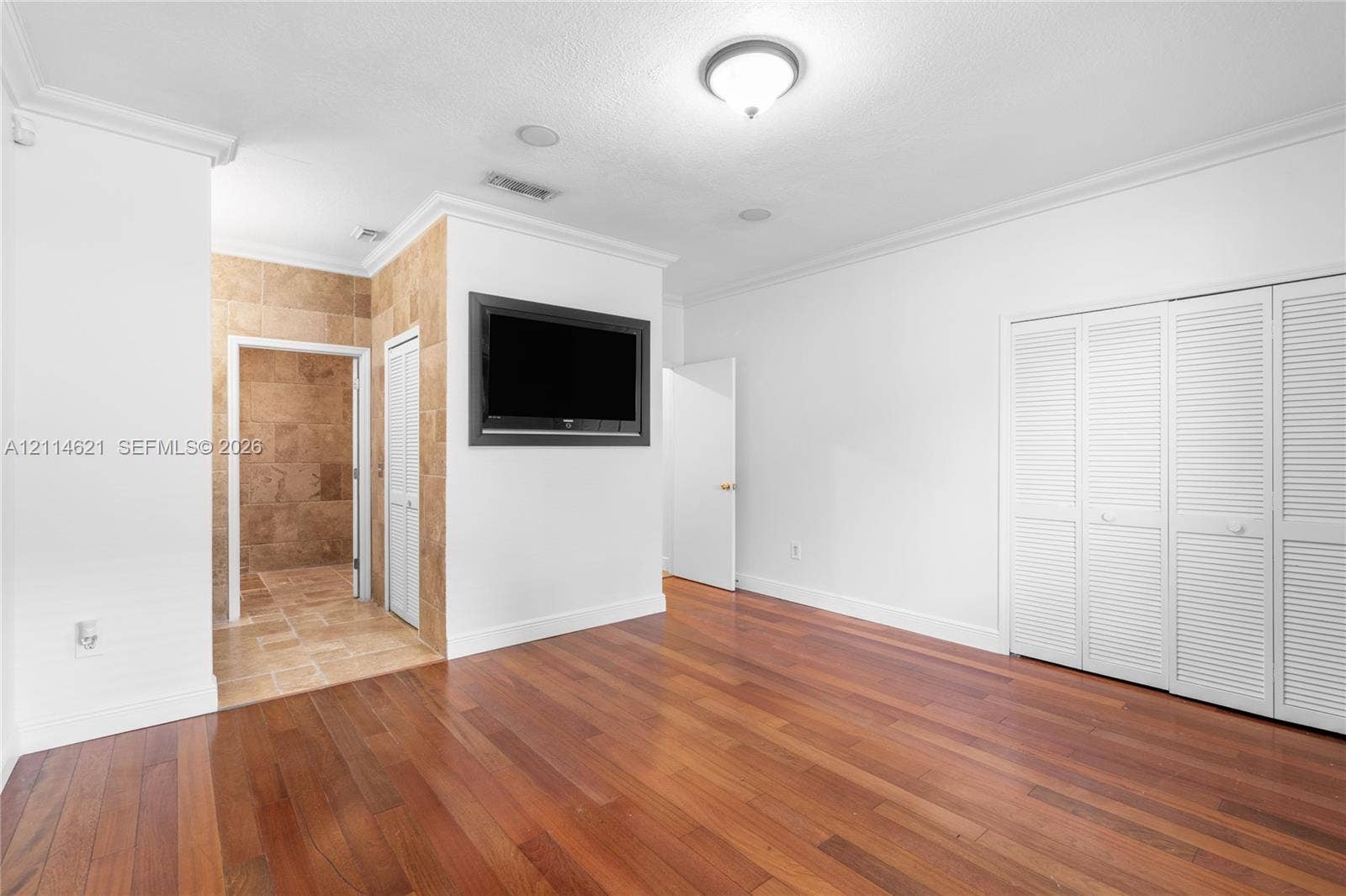 8978 NW 152nd Lane, #8978, Miami Lakes, Miami Lakes, FL 33018 Interior space featuring wood-finish flooring, white louvered closet doors, recessed ceiling lighting, and crown molding, with stone-tile finishes visible in the recessed area