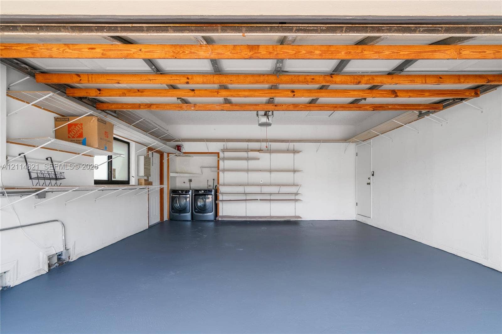 8978 NW 152nd Lane, #8978, Miami Lakes, Miami Lakes, FL 33018 Garage interior featuring exposed wood ceiling beams, painted concrete flooring, mounted metal shelving units, and built-in laundry appliances