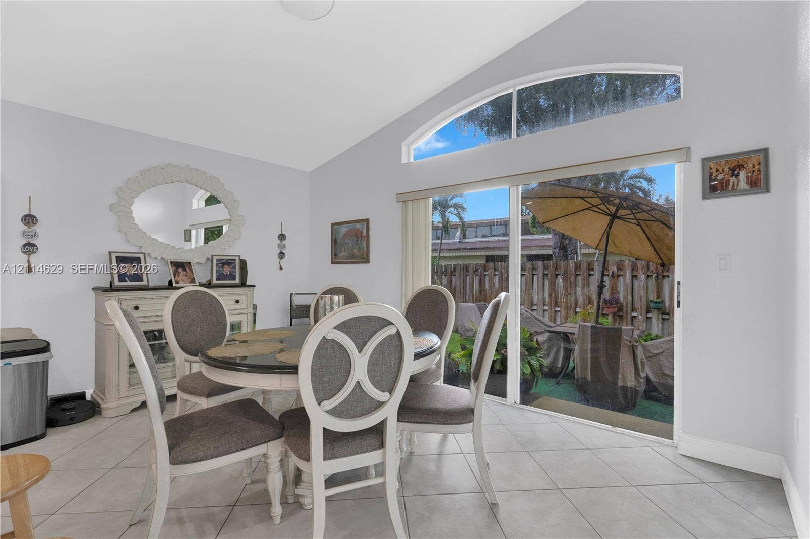Vaulted ceilings featuring a semi-circular arched transom window and sliding glass doors with direct patio access, complemented by large-format tile flooring
