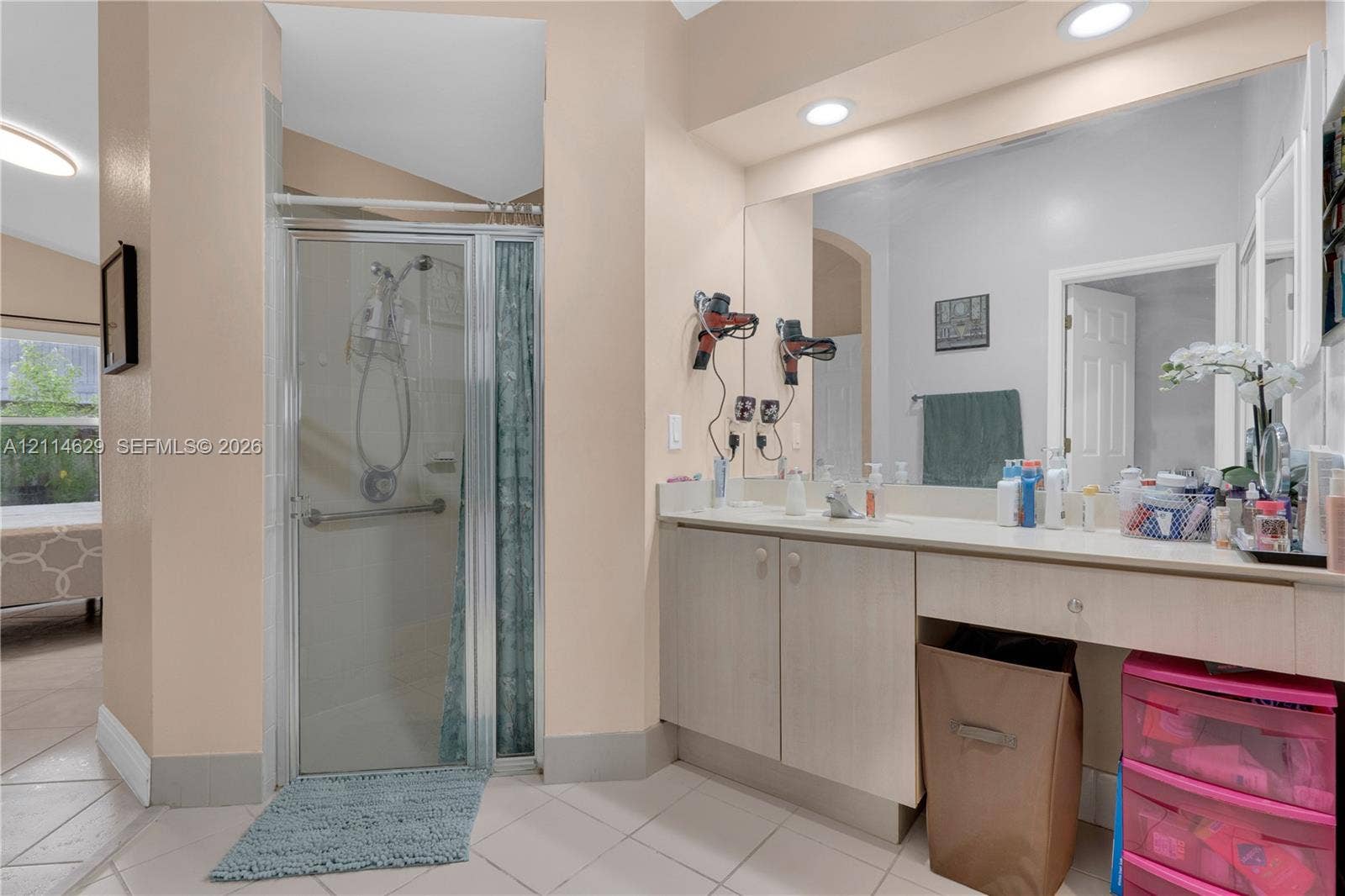 Bathroom featuring a vanity with wood-finish cabinetry, a full-width mirror, recessed lighting, and a glass-enclosed shower with tile flooring