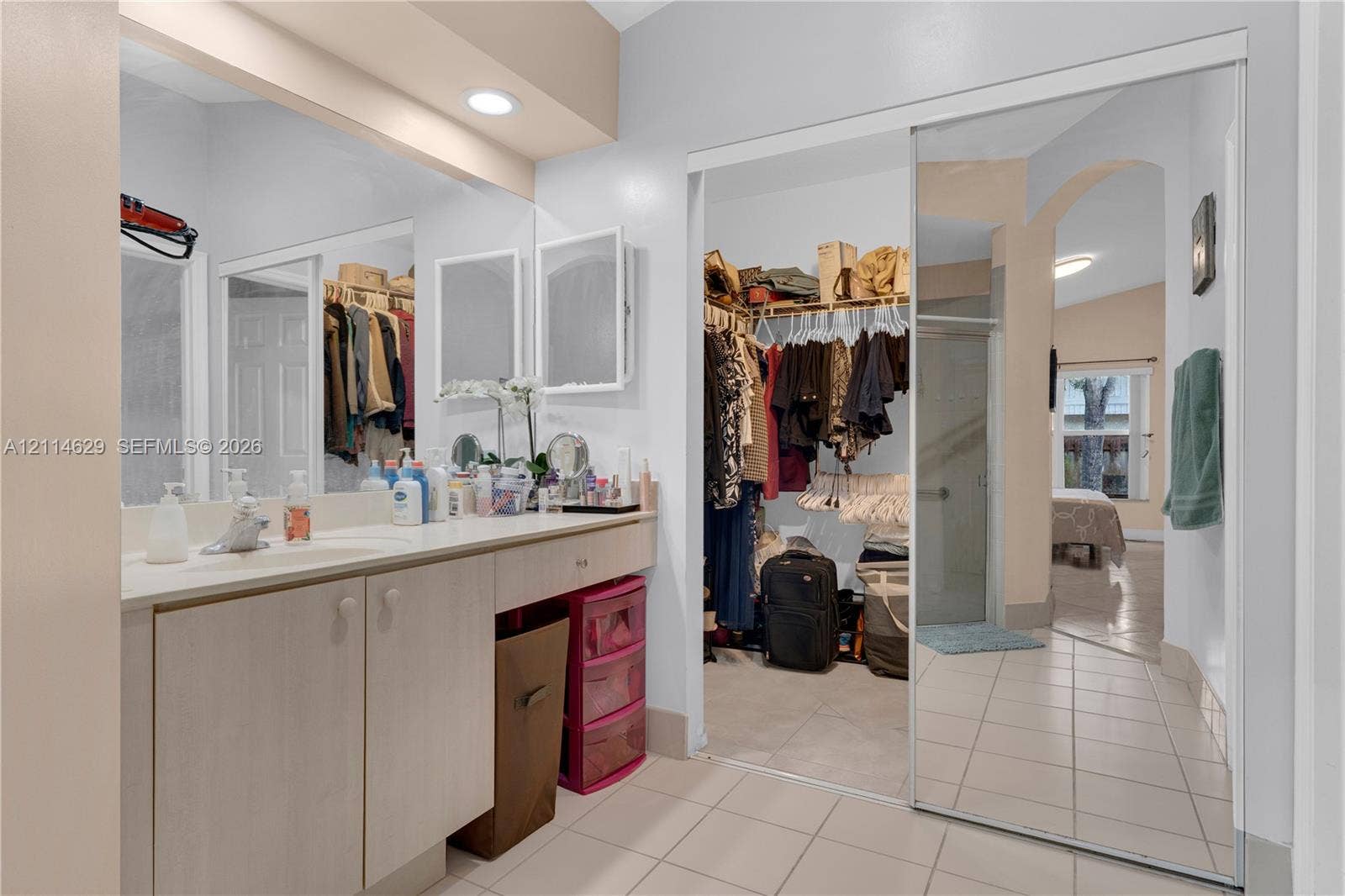 Vanity featuring neutral cabinetry and a solid surface countertop with a single-basin sink, accompanied by a large wall-to-wall mirror, recessed lighting, and mirrored sliding closet doors
